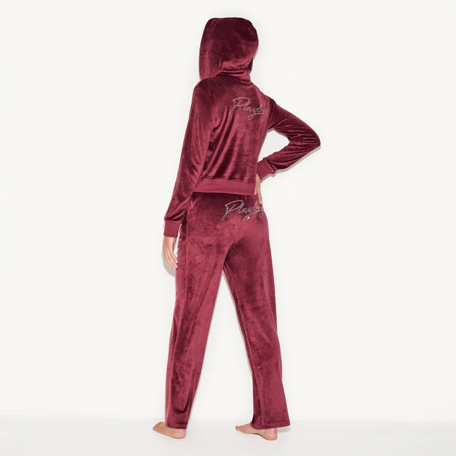 Woman wearing a burgundy velour hooded jacket and pants set with script embroidery on back