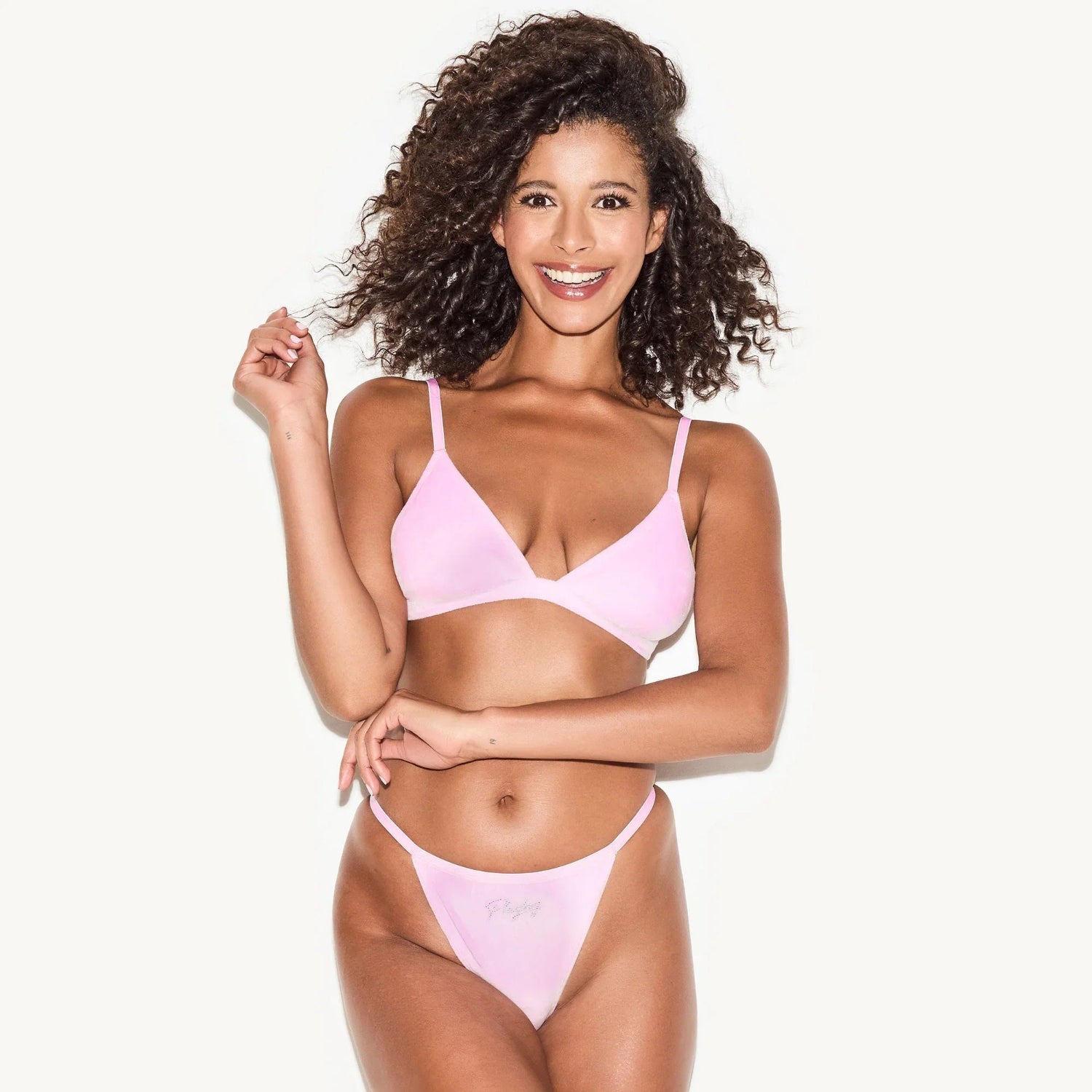 Woman modeling light pink velour thong and bralette lingerie set on white background