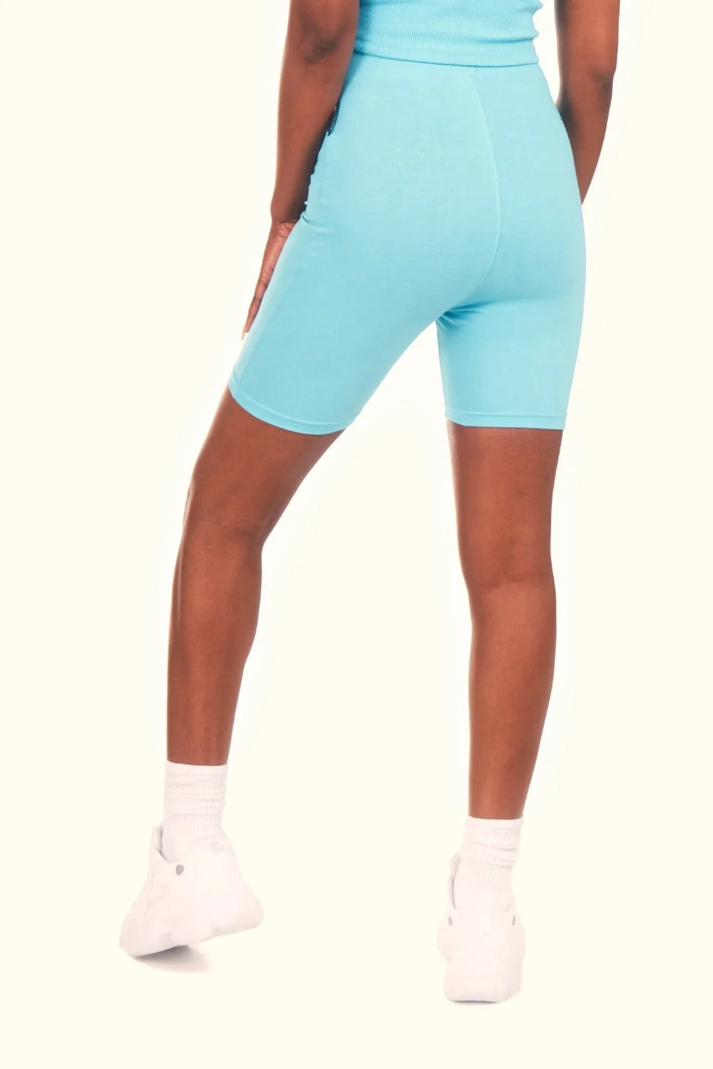 Woman wearing light blue biking shorts and white sneakers, seen from the back
