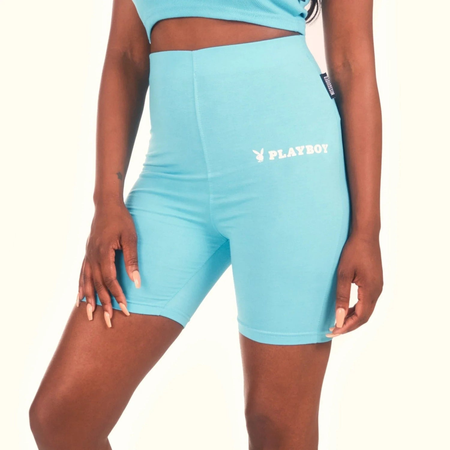 Woman wearing high-waisted light blue biker shorts with white Playboy logo print.