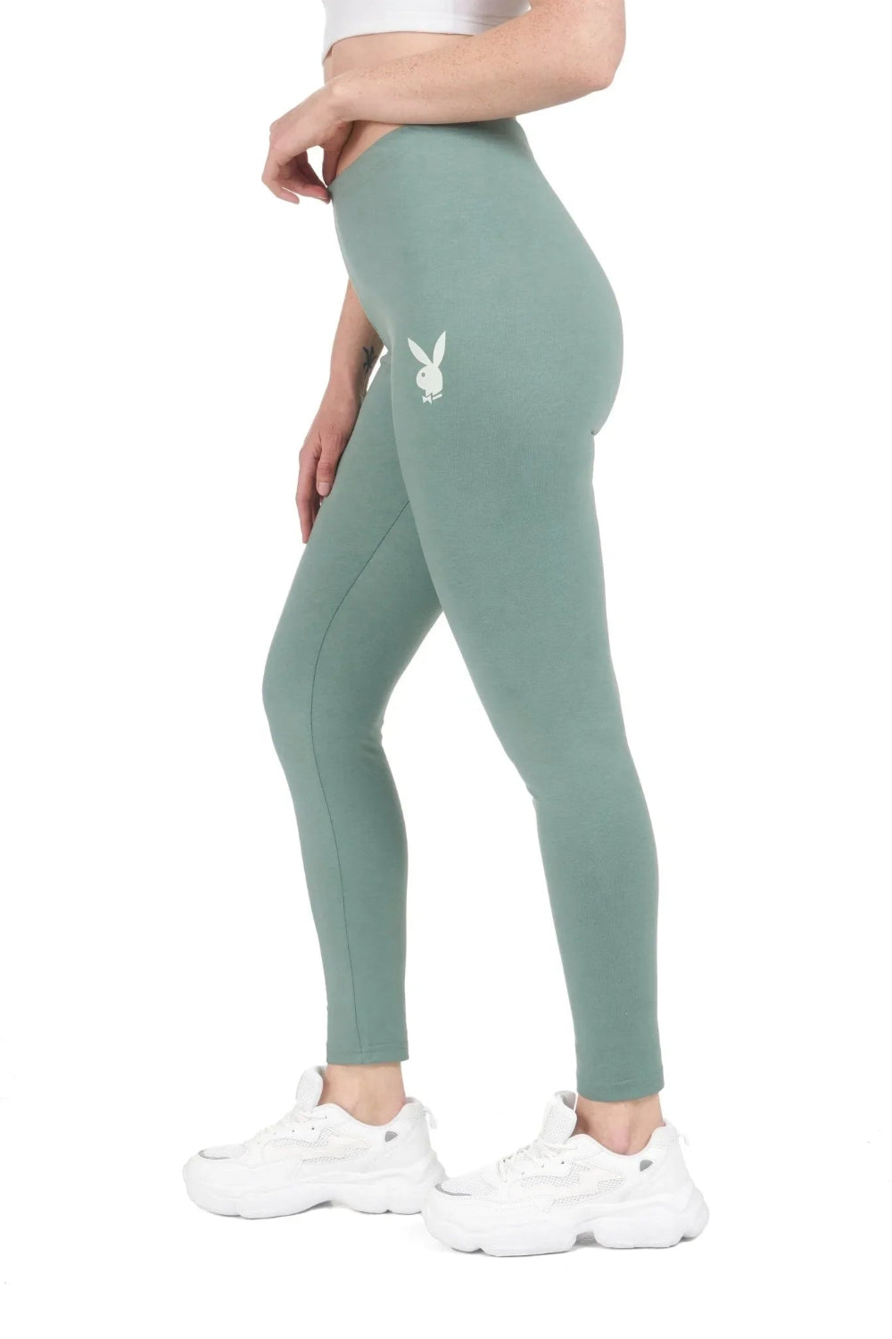 Woman wearing sage green high-waisted leggings with rabbit head logo, white sneakers