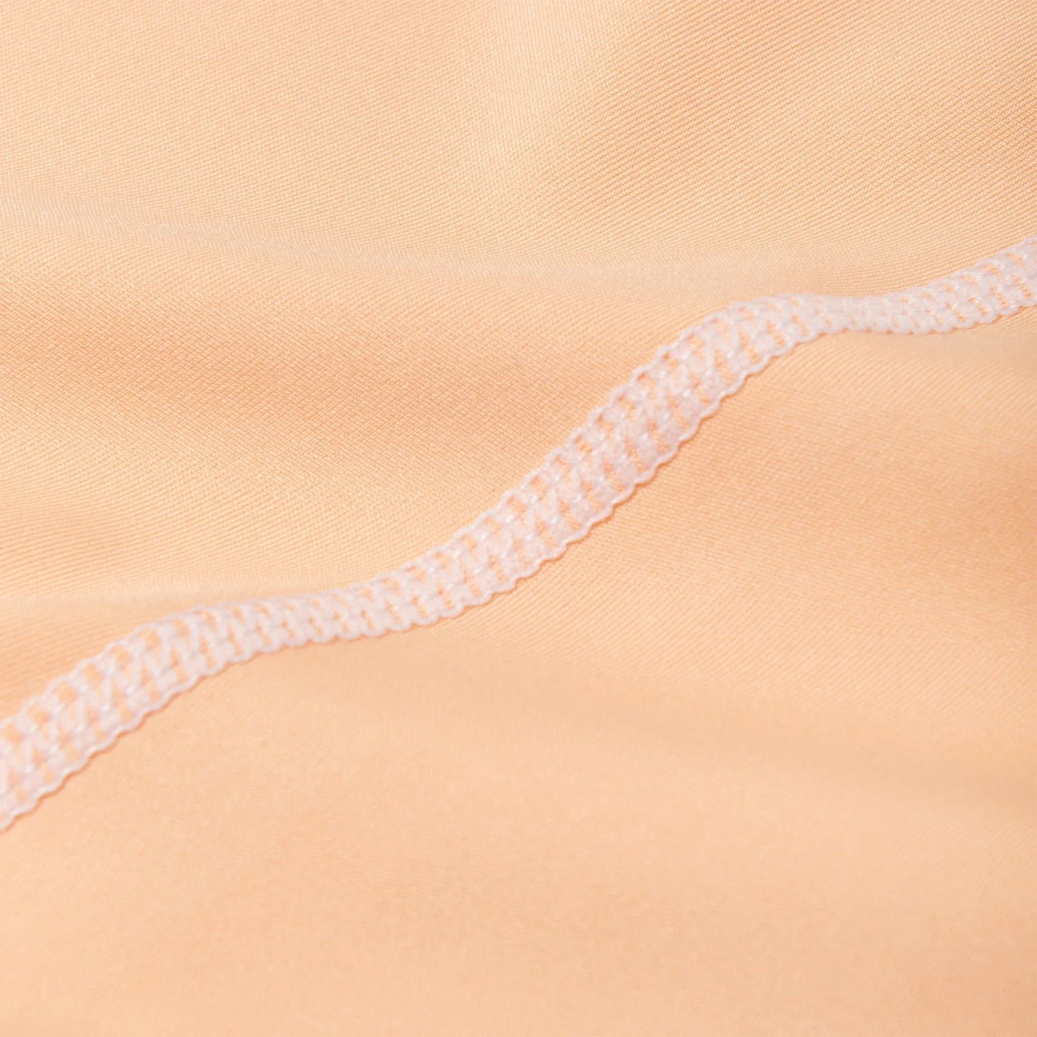 Close-up of peach activewear fabric with visible ruched seam and smooth texture.
