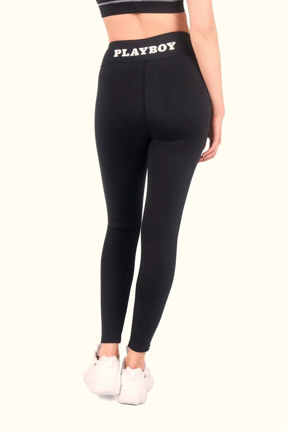 Woman wearing high-waisted black leggings with ruched waistband and white logo detail