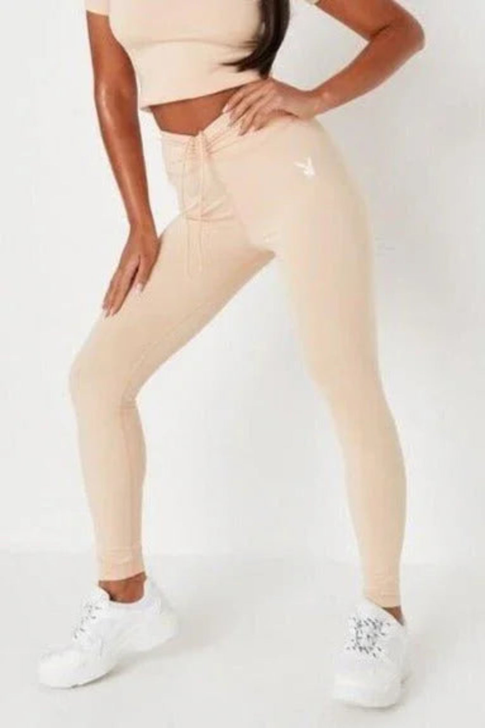 Woman wearing beige ruched waistband leggings with white bunny logo, white sneakers
