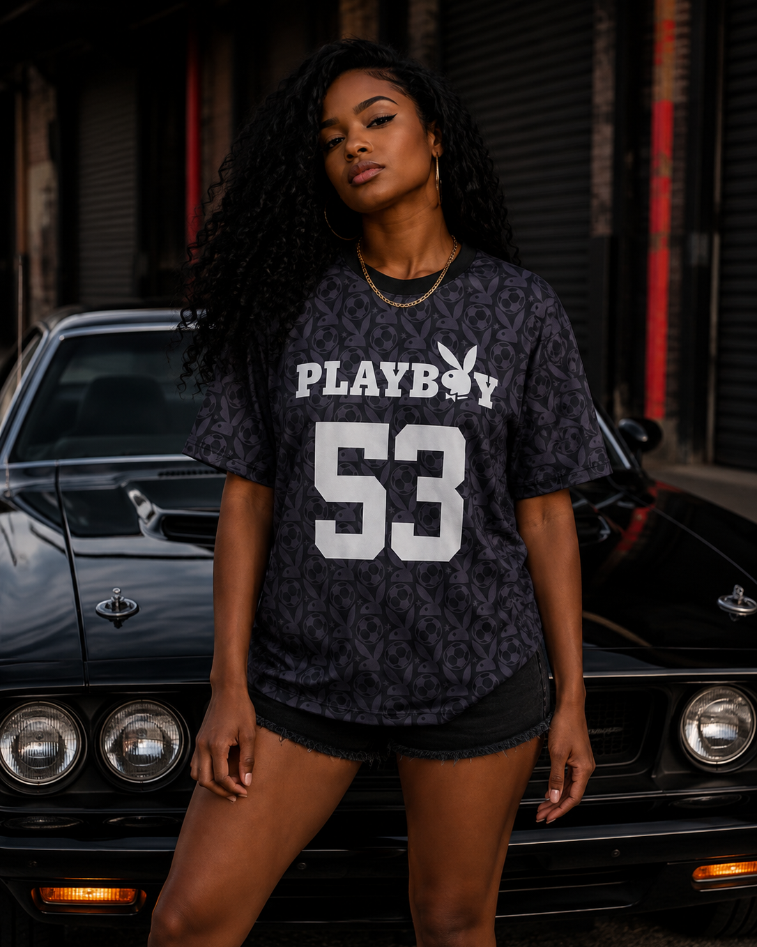 A woman stands in front of a black classic car wearing a dark patterned Playboy t-shirt with 'PLAYBOY 53' printed in white, paired with black denim shorts. #Streetwearwomen
