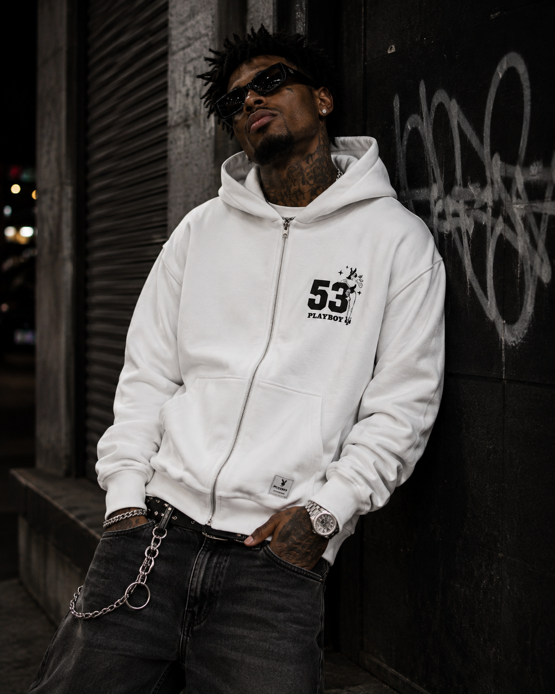 A man wearing a white zip-up hoodie with a black '53' logo on the left chest, standing in front of a graffiti-covered metal shutter. #Streetwearmen