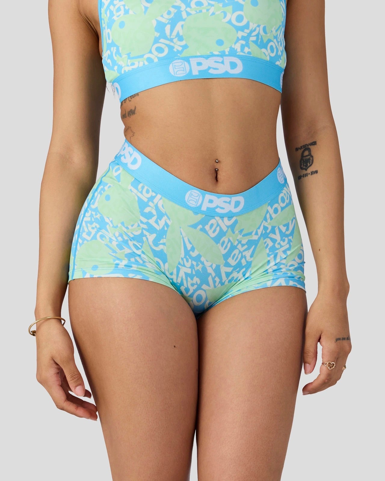 A model wearing a two-piece swimsuit with a light blue and mint green abstract pattern, featuring the brand name 'PSD' printed on the waistbands.