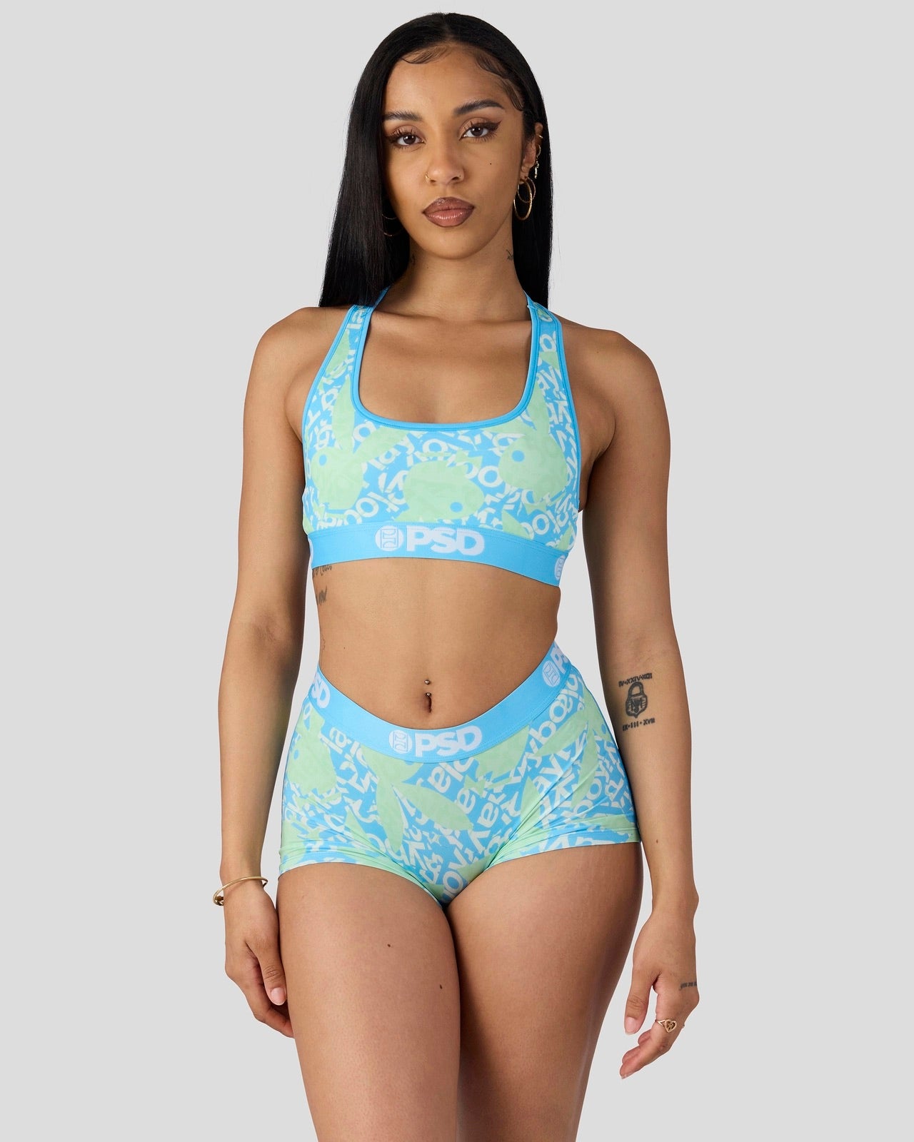 A woman modeling a two-piece athletic set consisting of a sports bra and matching high-waisted shorts in a light blue and lime green color-blocked design with a white abstract pattern. The brand name 'PSD' is visible on the waistband of the shorts and the underband of the sports bra.