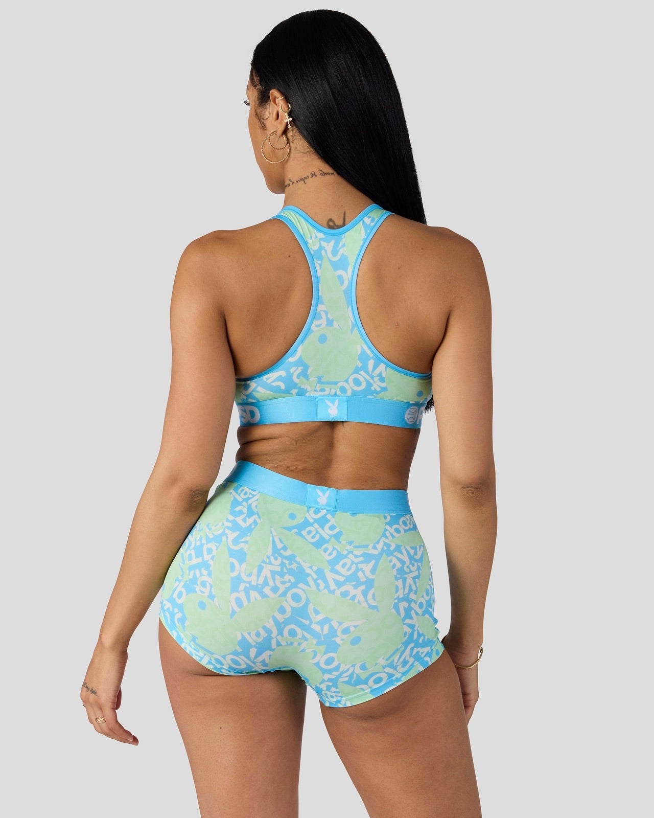 A woman shown from the back wearing a matching two-piece activewear set with a light green and blue abstract pattern, photographed against a solid light gray studio background.