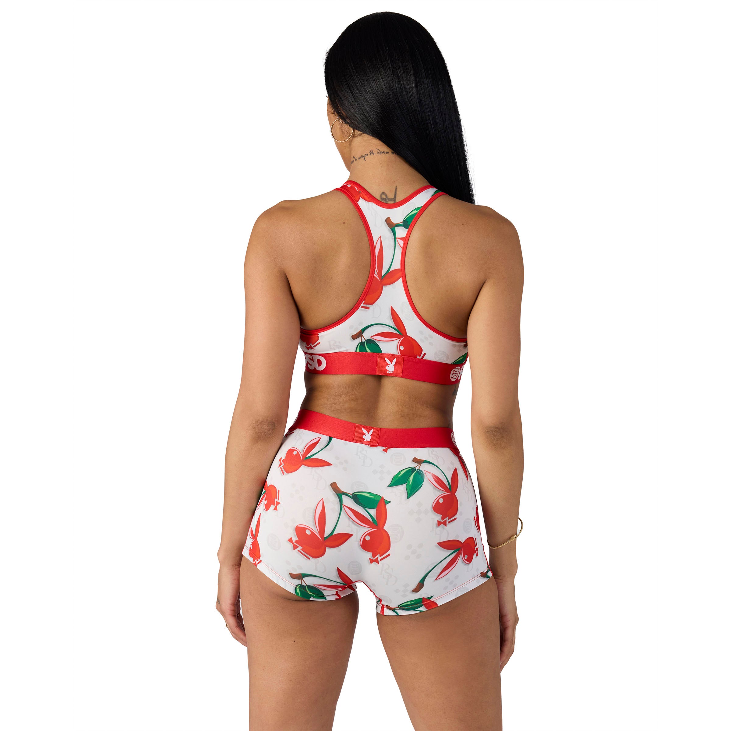 Woman modeling Playboy sports bra and shorts set with red and green bunny logo print, back view