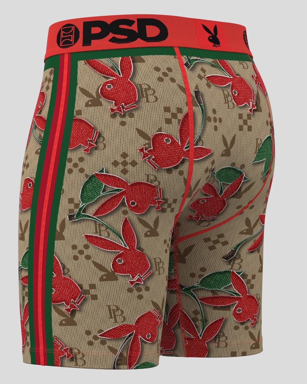 A pair of boxer briefs featuring a beige monogram pattern with red bunny motifs, green leaves, and red side stripes. The waistband is bright red with 'PSD' and the Playboy bunny logo printed in black.
