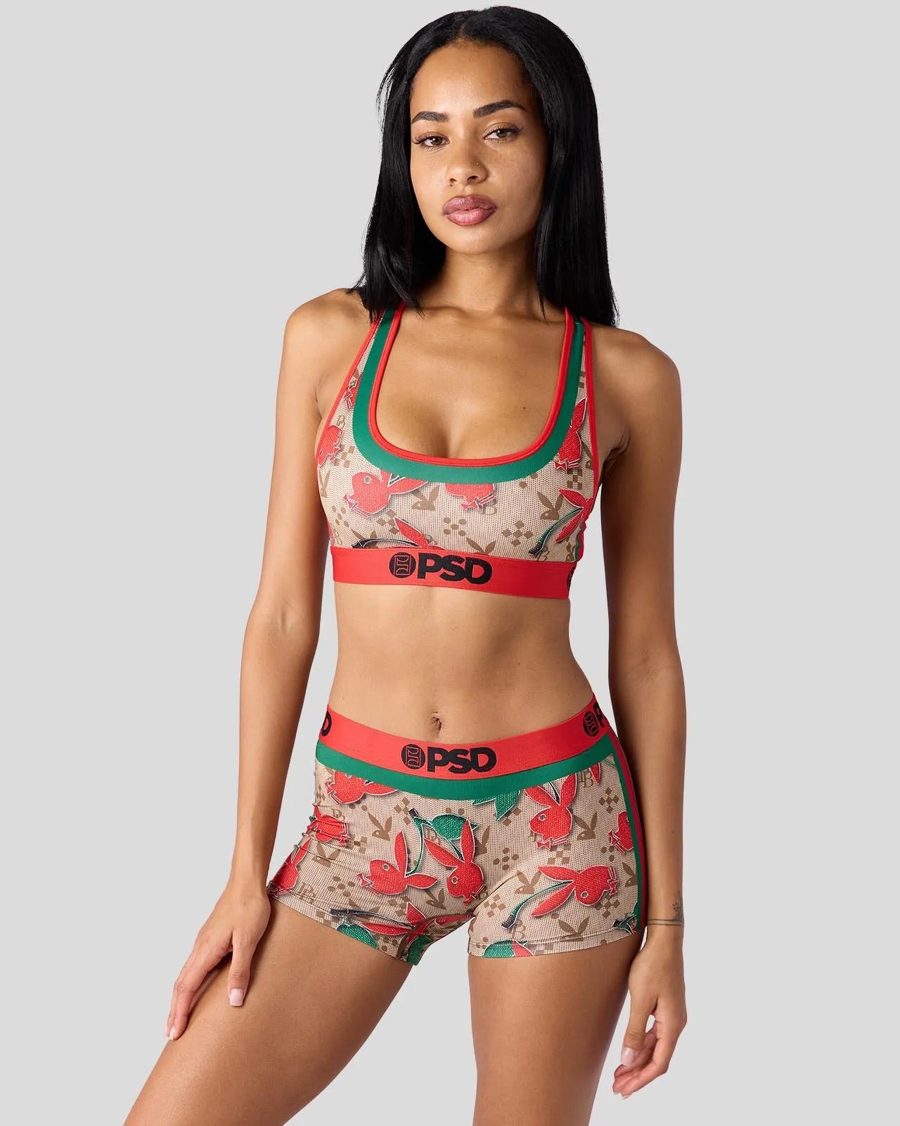 A woman modeling a matching two-piece athletic set featuring a beige floral print with red and green trim, including a sports bra and shorts with a red waistband and 'PSD' logo.