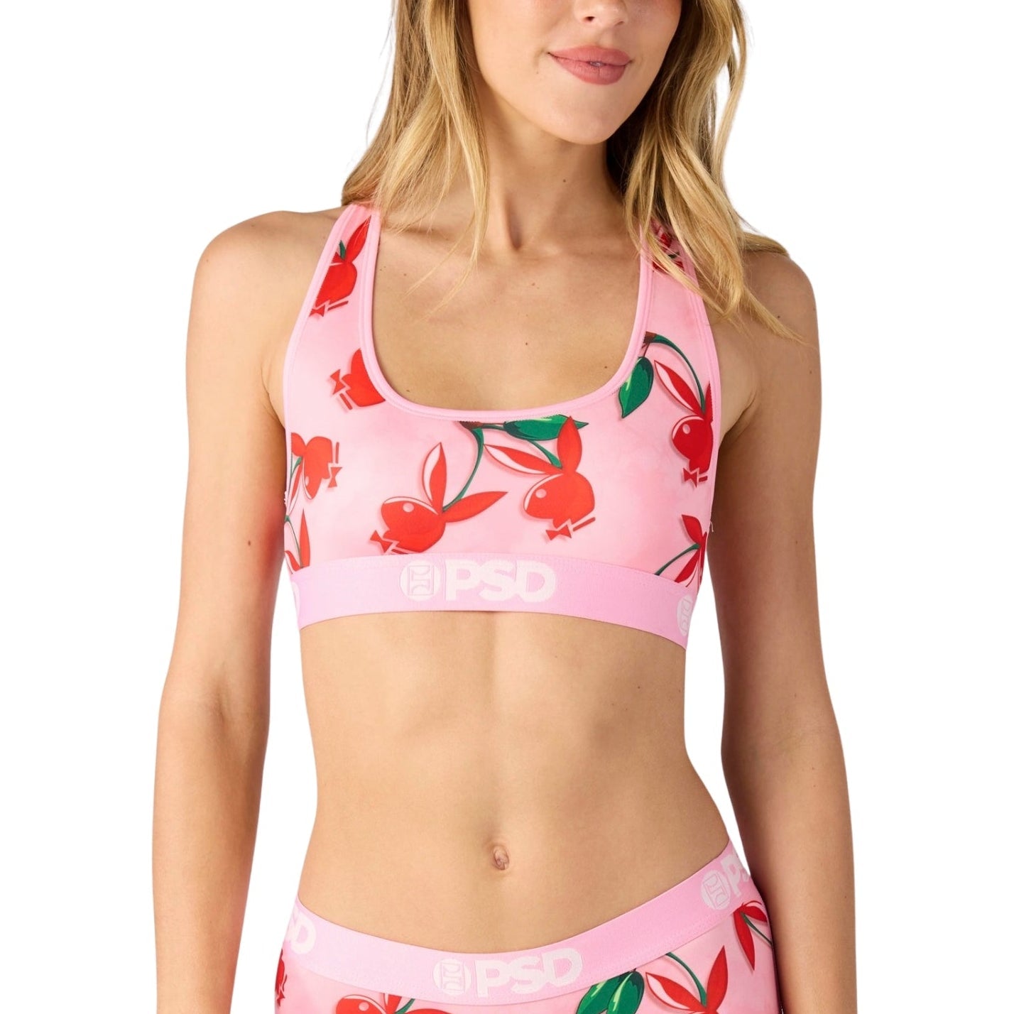 Woman wearing a pink sports bra and shorts with cherry pattern on a white background