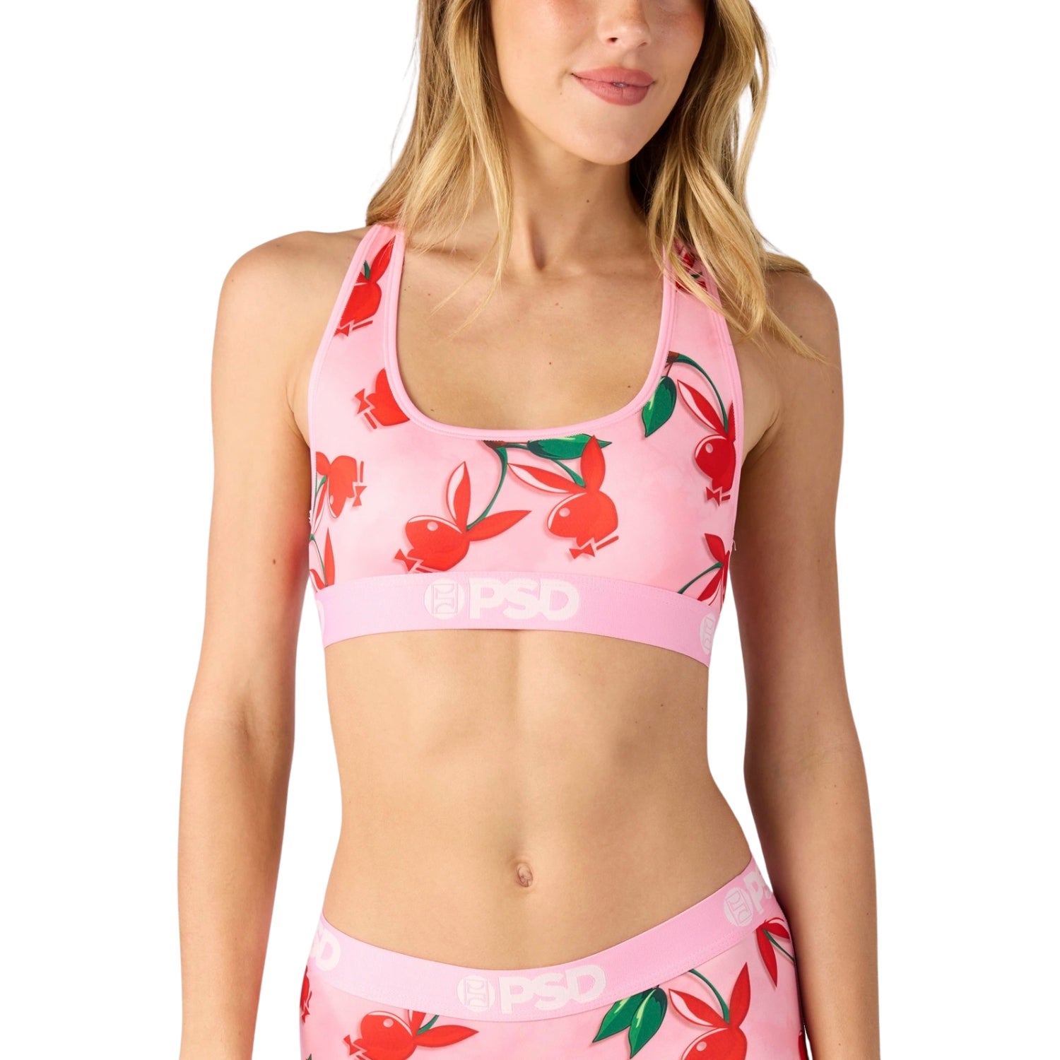 Woman wearing a pink sports bra and shorts with cherry pattern on a white background