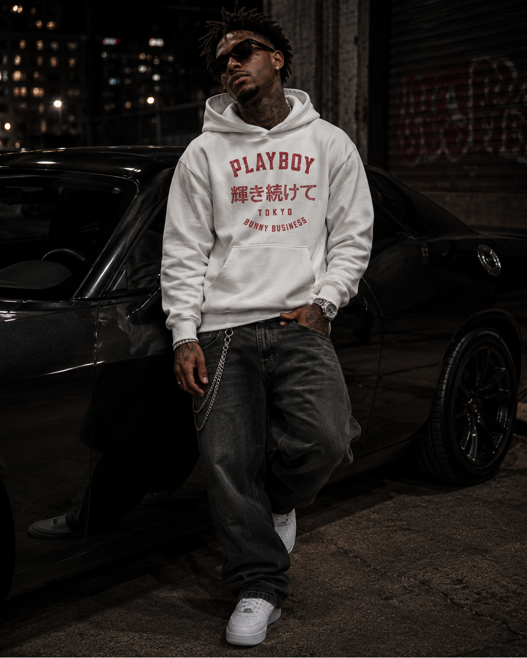 A man wearing a white Playboy hoodie with red Japanese text and 'PLAYBOY' stands next to a black car at night. #Streetwearmen