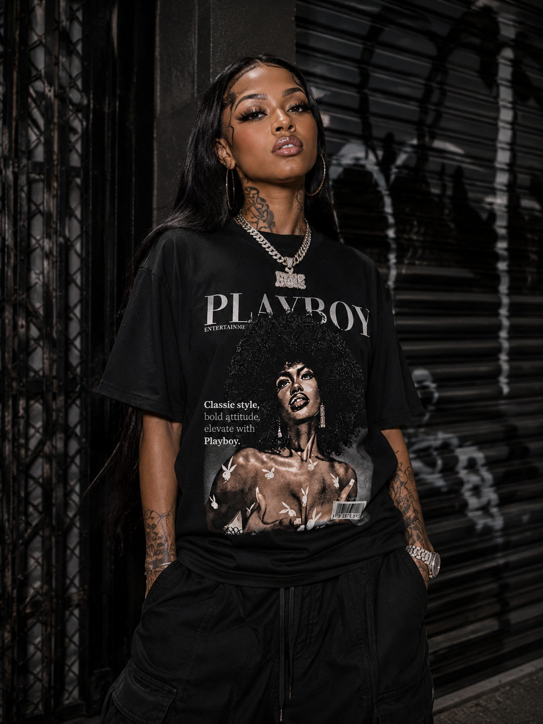 A woman wearing a black oversized graphic t-shirt with a vintage-style Playboy print, paired with black cargo pants, standing in front of a dark metal shutter.  #Streetwearwomen