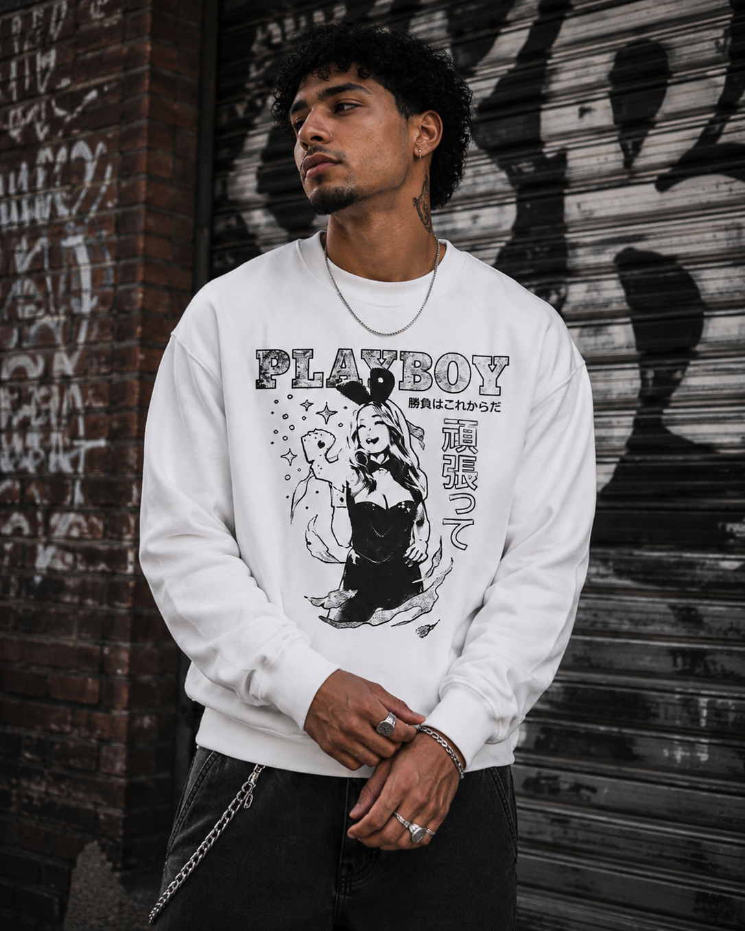 A man wearing a white Playboy crewneck sweatshirt with a black graphic print, standing in front of a graffiti-covered metal shutter. #Streetwearmen