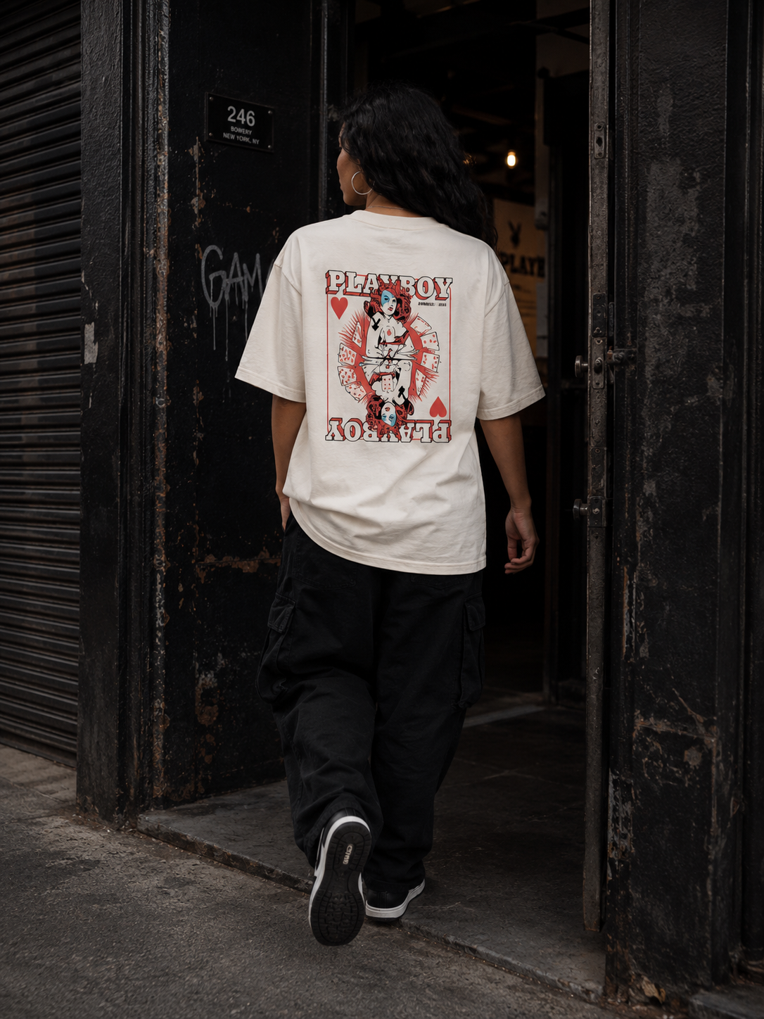 A person viewed from behind wearing an off-white graphic t-shirt with a red and black 'PLANBOY' design, paired with black cargo pants, walking through a dark doorway. #Streetwearwomen
