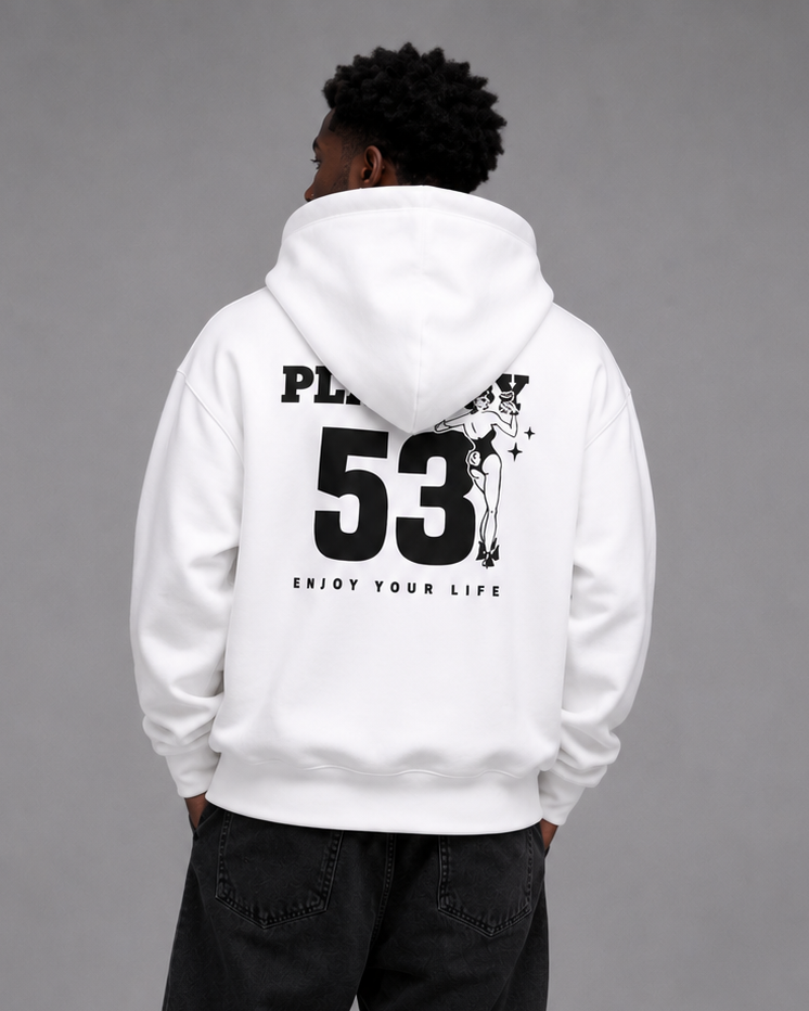 A man viewed from behind wearing a white pullover hoodie with a large black graphic print on the back, paired with black jeans and white sneakers, against a solid gray studio background.