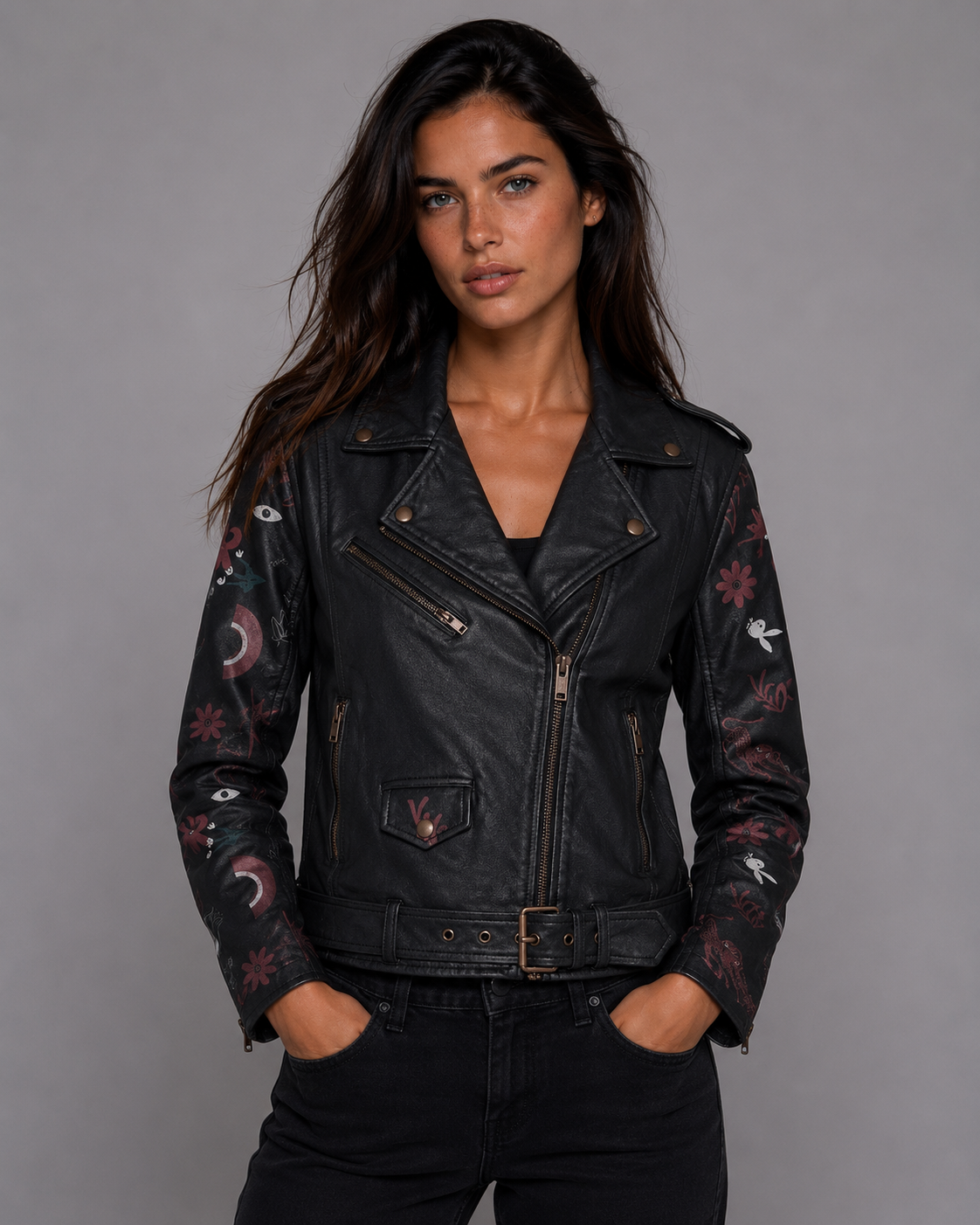 A woman modeling a black leather moto jacket with celestial and floral embroidery on the sleeves, paired with black jeans against a solid gray studio background. #Women