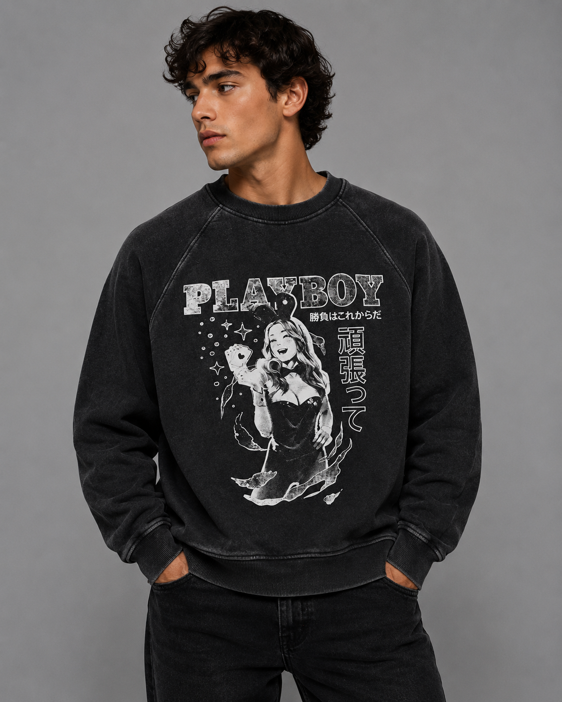 A man wearing a faded black graphic sweatshirt with a white Playboy print on the front, paired with black jeans, photographed against a solid gray studio background.