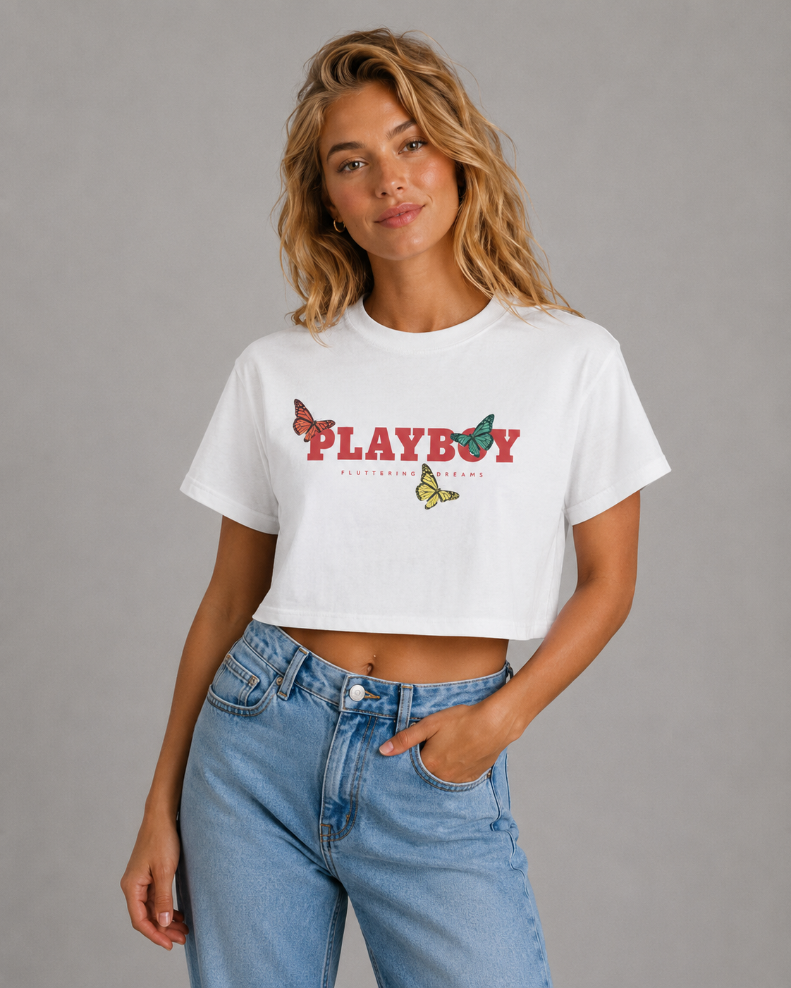 A woman modeling a white cropped t-shirt with a red 'PLAYBOY' graphic and butterfly details, paired with light-wash blue jeans against a solid gray studio background. #Women