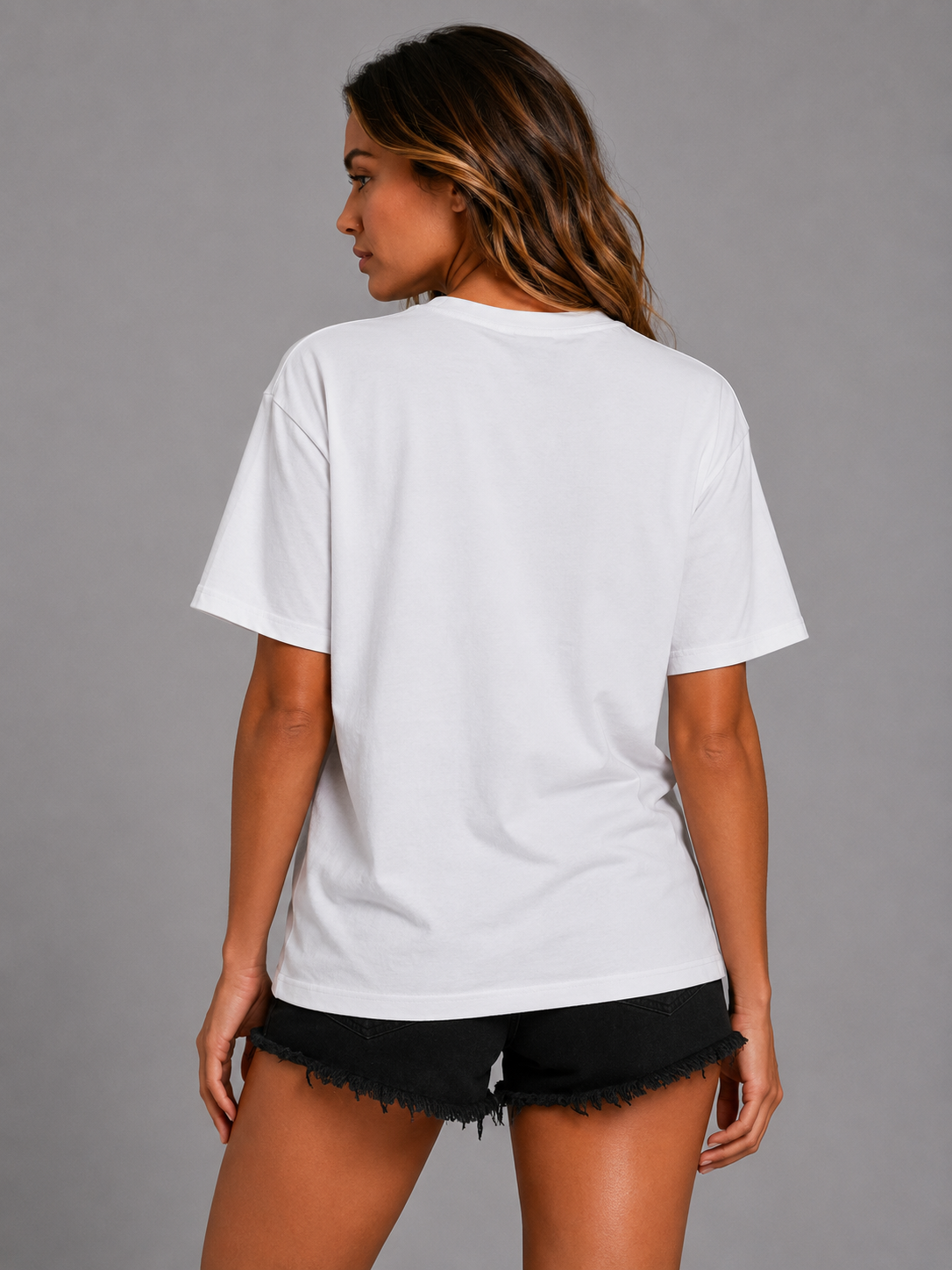 A woman shown from the back wearing an oversized white short-sleeve t-shirt and black frayed denim shorts, photographed against a solid gray studio background. #Women