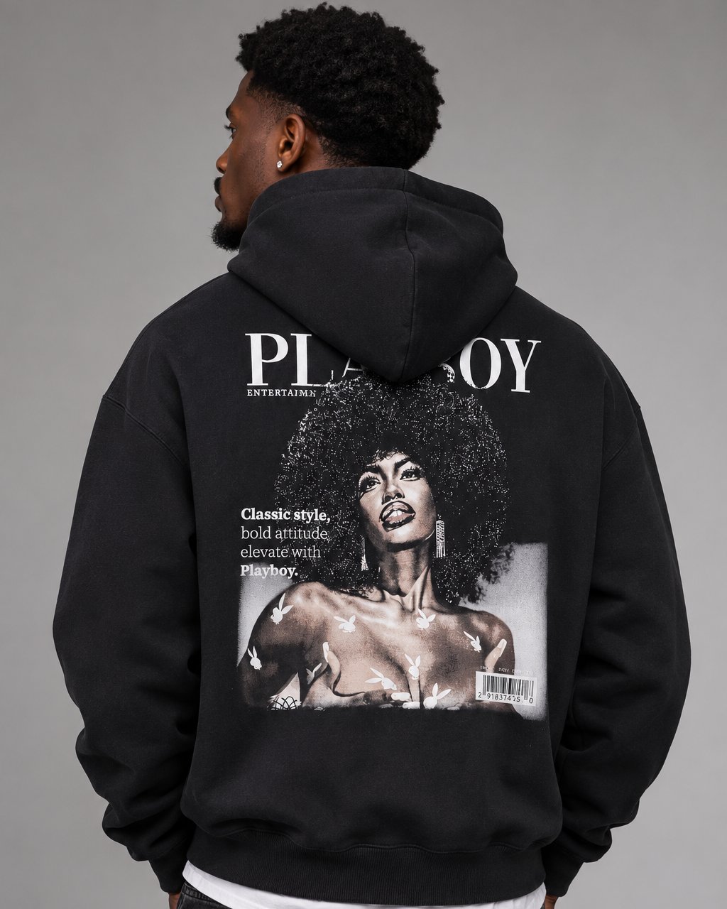 A man shown from the back wearing a black hoodie with a large Playboy magazine cover graphic printed on the back, paired with dark jeans against a neutral gray studio background.