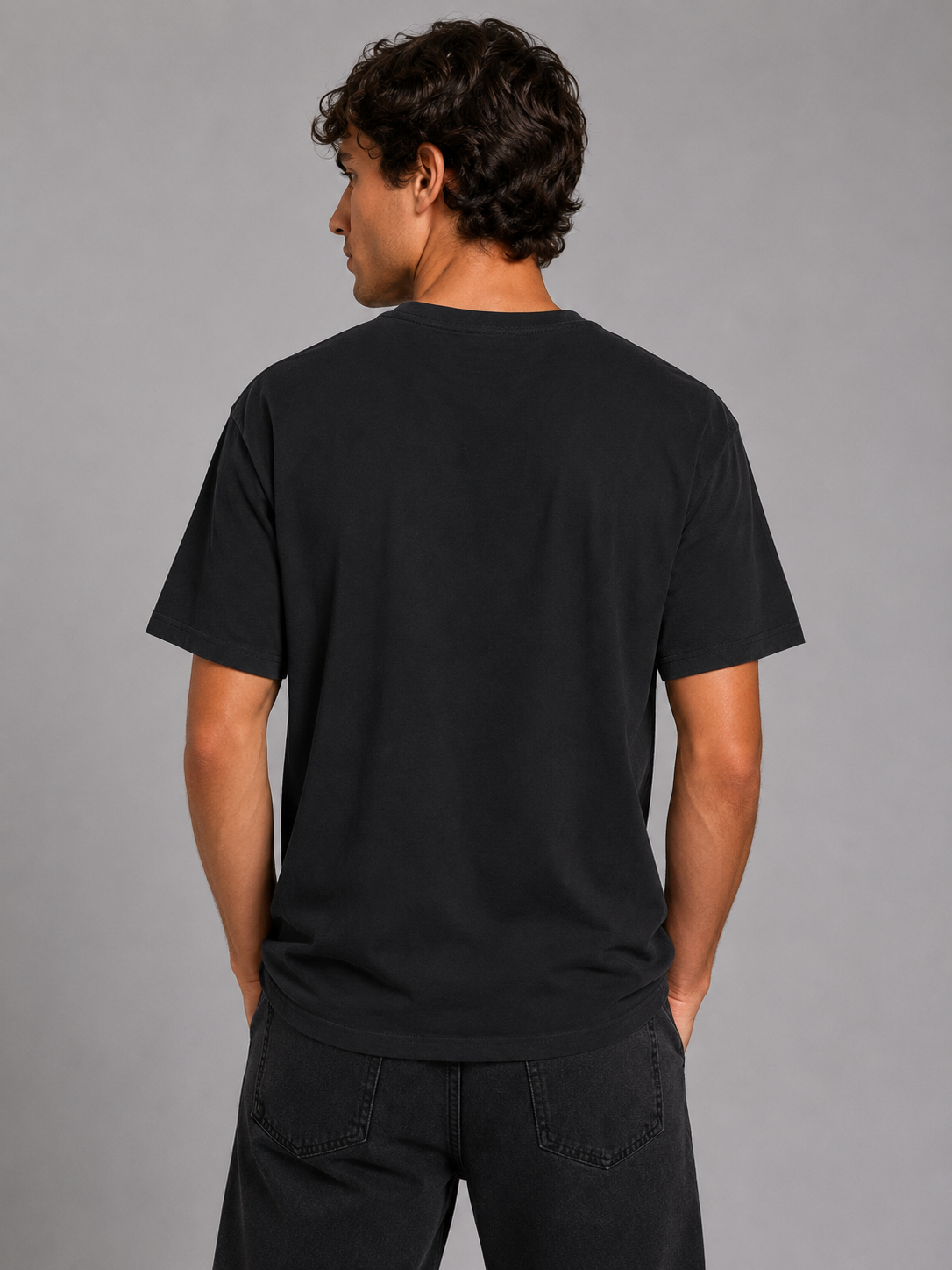 A man wearing a plain black short-sleeve t-shirt, shown from the back against a solid gray studio background.
