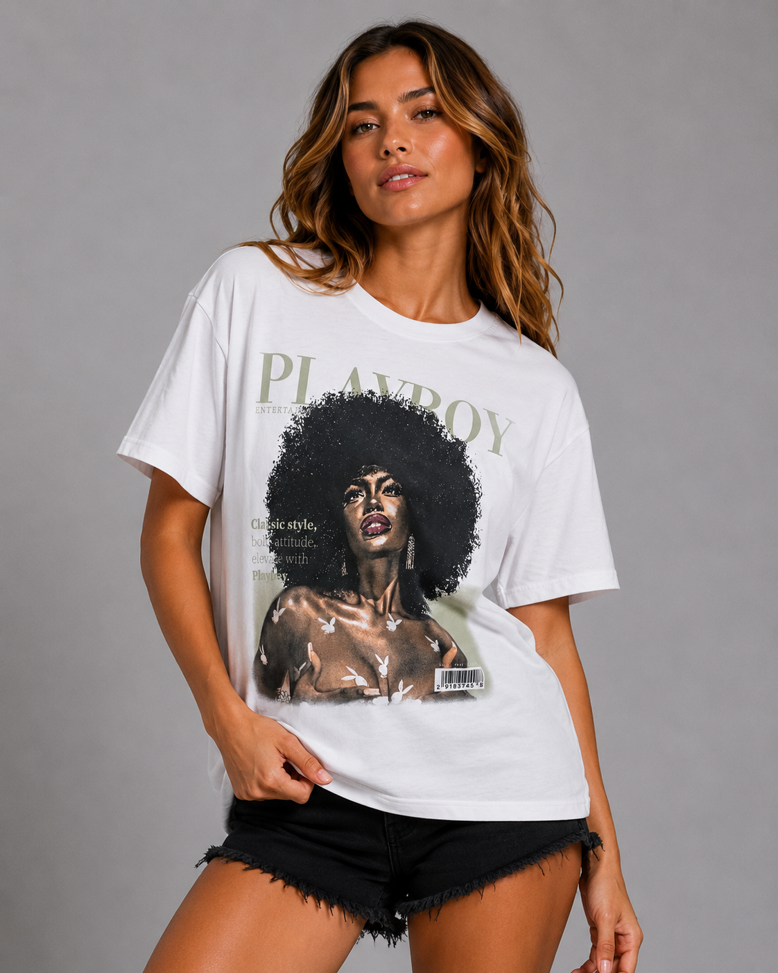 A woman modeling a white Playboy graphic t-shirt with a large vintage-style print of a woman with an afro and the word 'PLAYBOY' across the chest, paired with black frayed denim shorts against a solid gray studio background. #Women