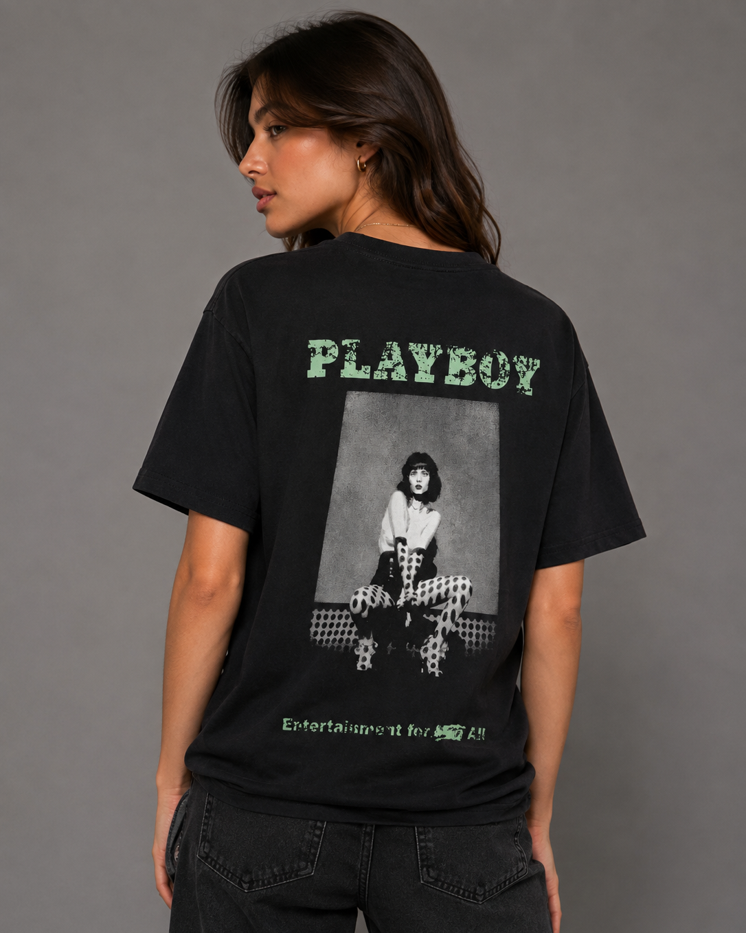 A woman shown from the back wearing a black oversized graphic T-shirt with a large grayscale photo print and green 'PLAYBOY' text on the back, photographed against a plain gray studio background. #Women