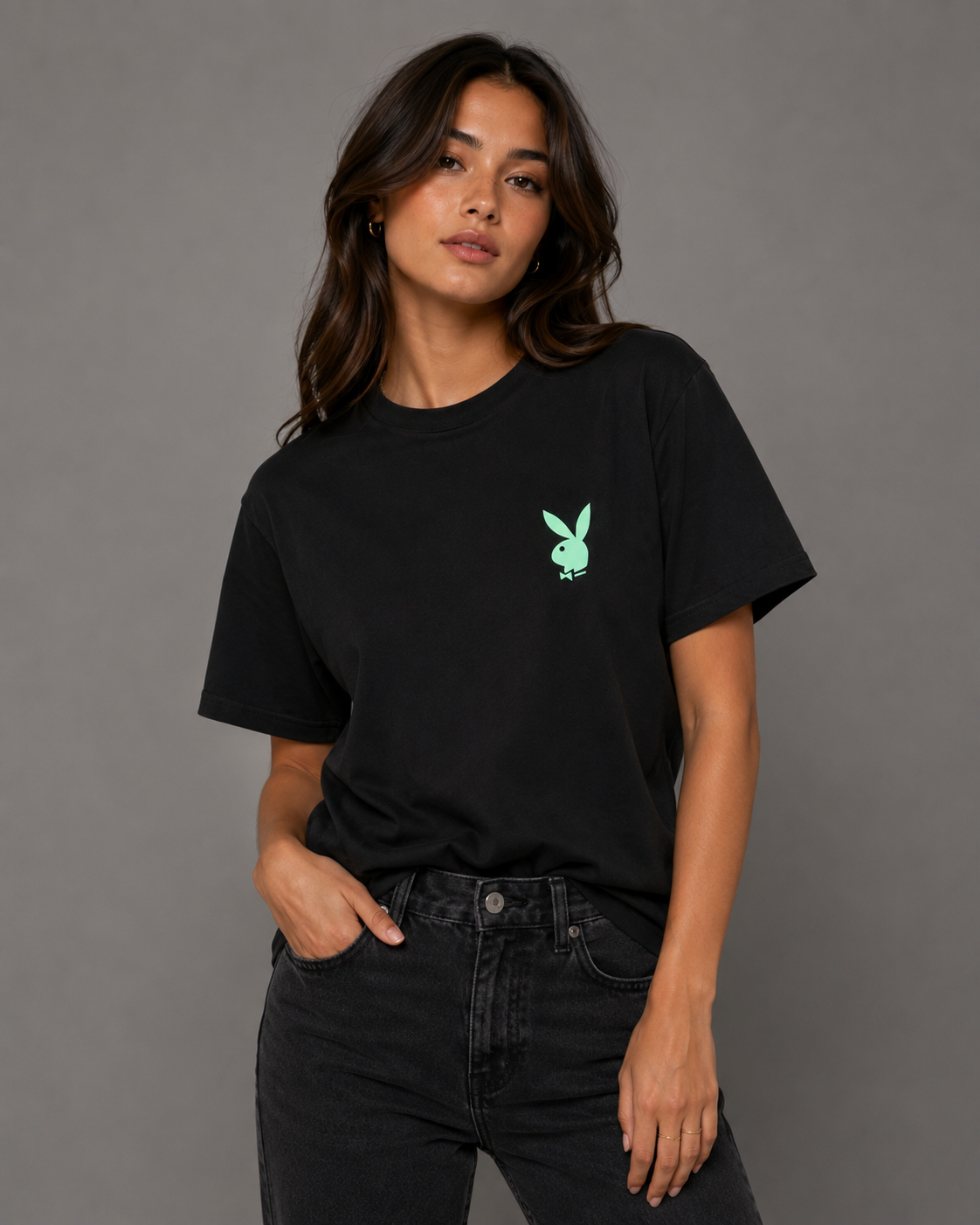 A woman modeling a black short-sleeve crewneck t-shirt with a small mint green Playboy bunny logo on the left chest, paired with black jeans against a solid gray studio background. #Women