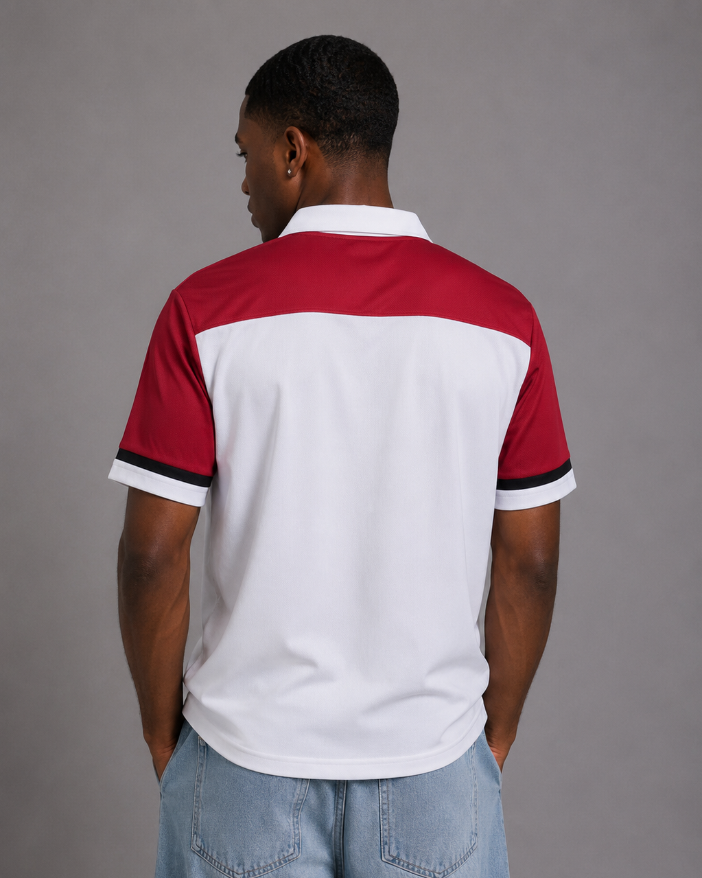A man viewed from behind wearing a short-sleeve polo shirt with a color-blocked design in red, white, and black, paired with light blue jeans against a solid gray studio background.