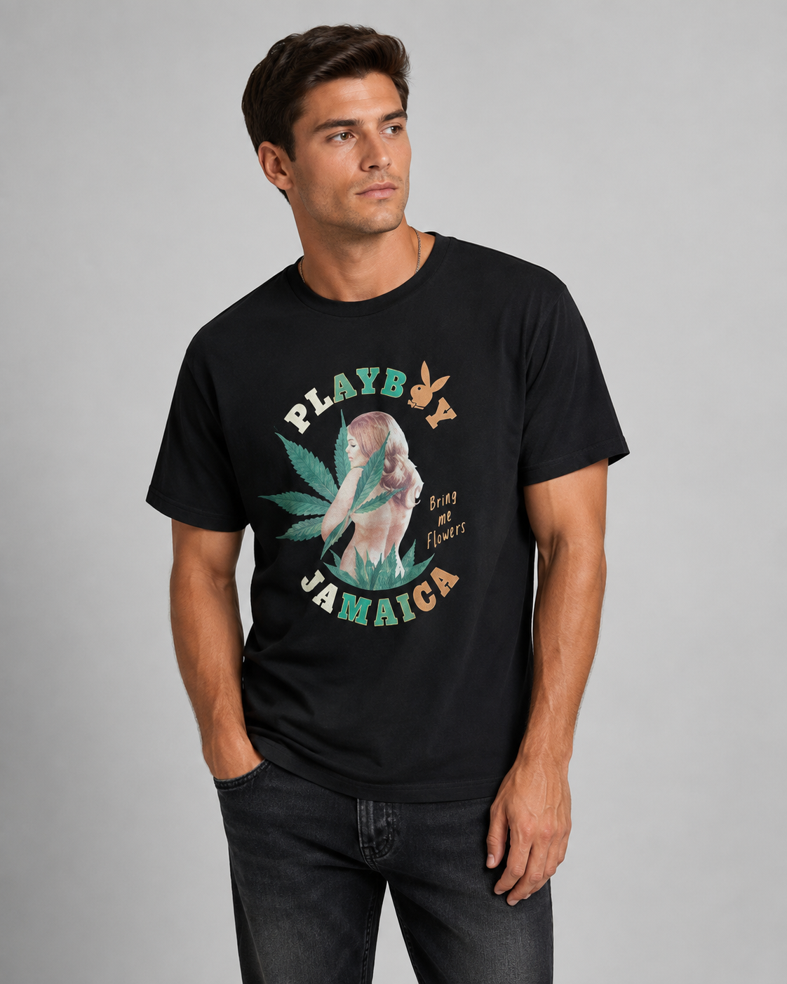 A man wearing a black short-sleeve graphic t-shirt with a 'Playb Jamaicag' design featuring a woman's profile, a cannabis leaf, and a bunny logo, paired with dark gray jeans against a solid gray studio background.