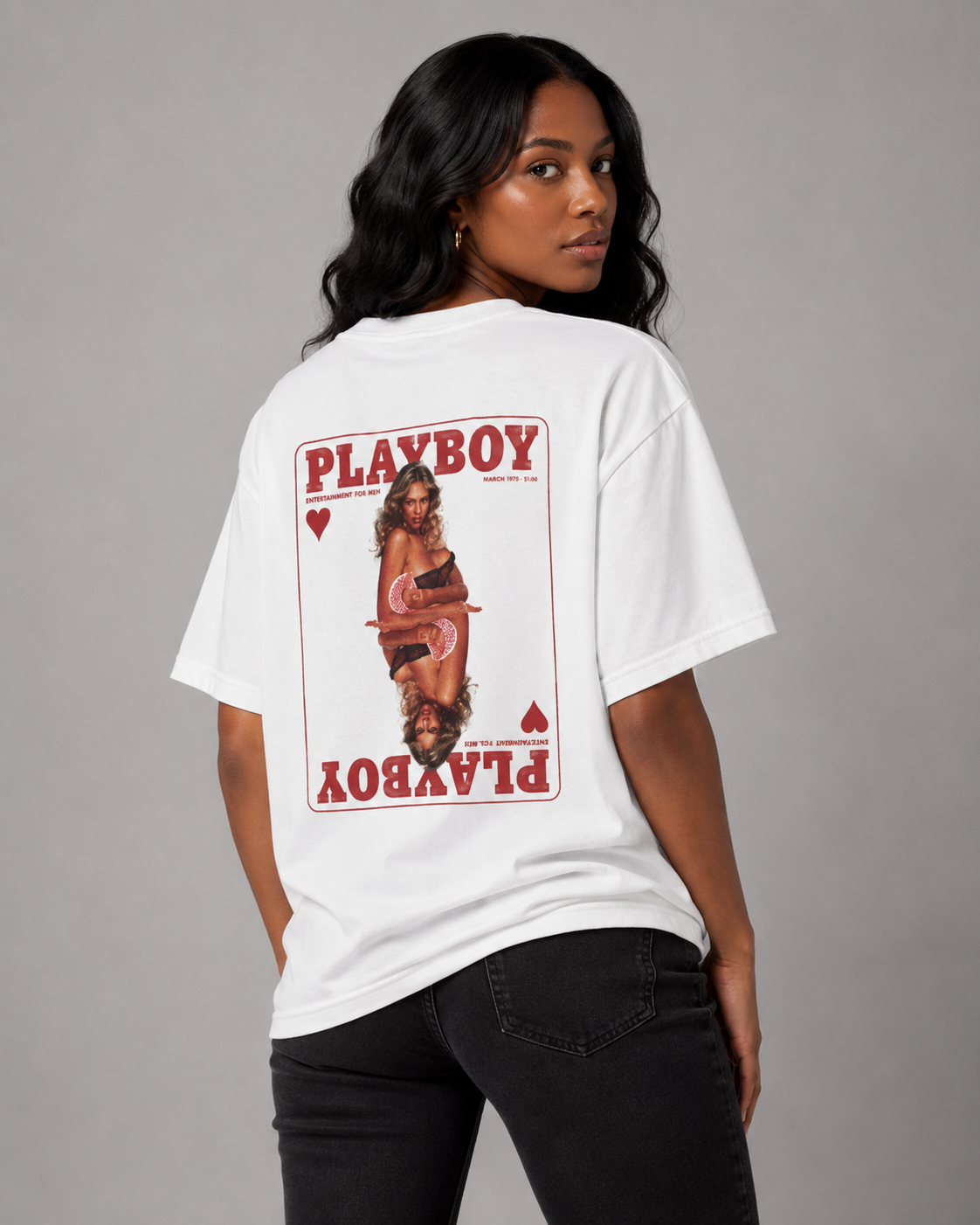 A woman wearing a white oversized Playboy t-shirt with a large red and black playing card graphic on the back, paired with black jeans, photographed against a neutral gray studio background. #Women