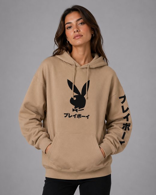 A woman modeling a beige pullover hoodie with a black Playboy bunny logo and Japanese text on the front, plus black Japanese text down one sleeve, against a plain gray studio background.