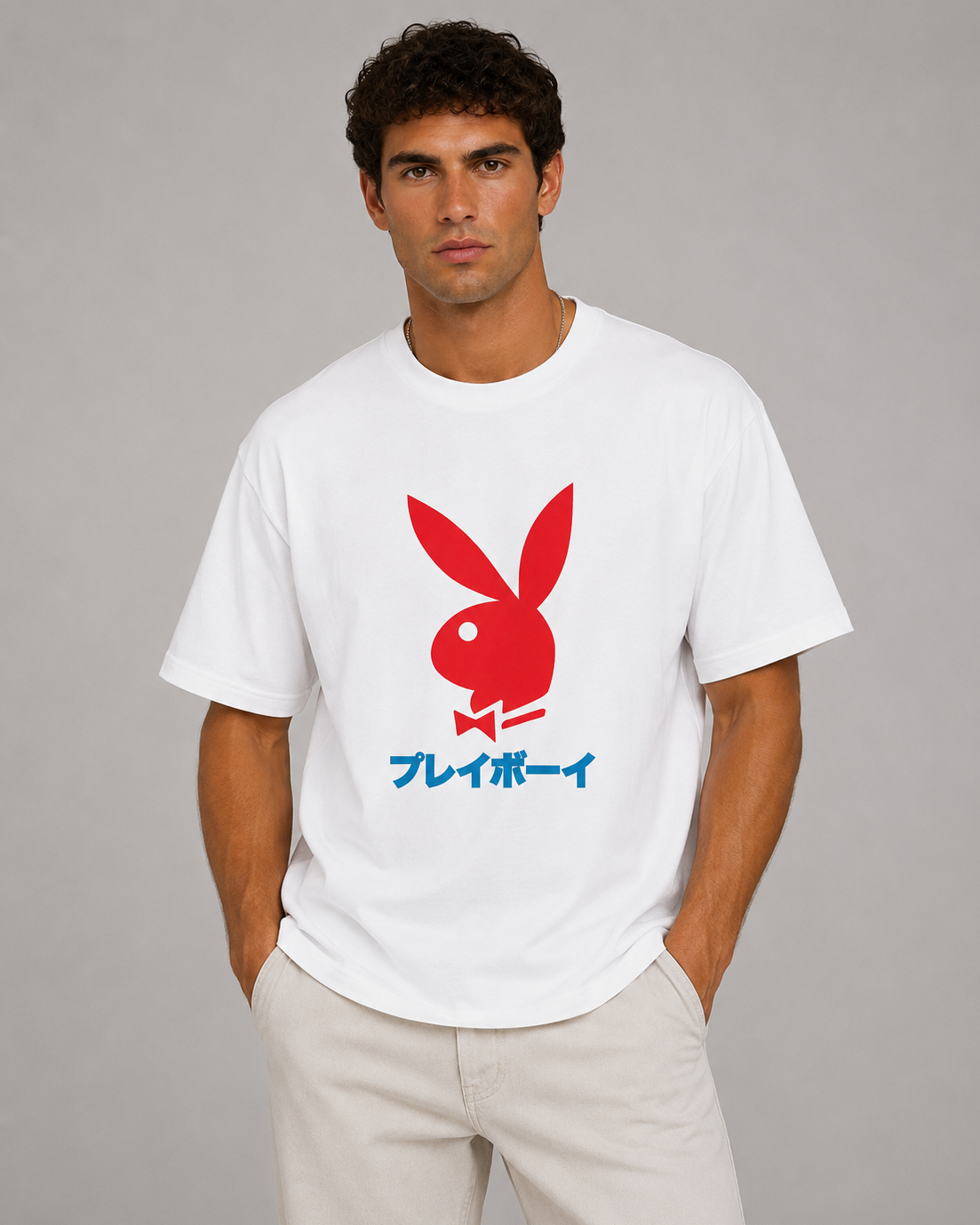 A man wearing a white short-sleeve t-shirt with a red Playboy bunny logo and blue Japanese text on the front, paired with light beige pants, against a solid gray studio background.