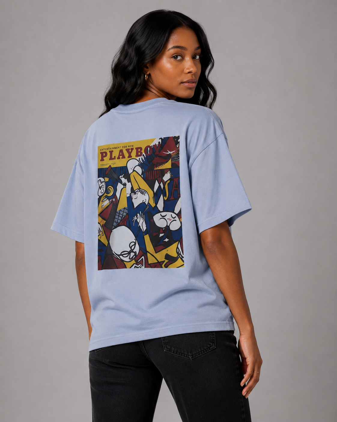 A woman modeling a light blue oversized T-shirt from the back, featuring a large graphic print of the Playboy Playmates logo and illustrations. She is wearing black jeans against a plain gray studio background. #Women