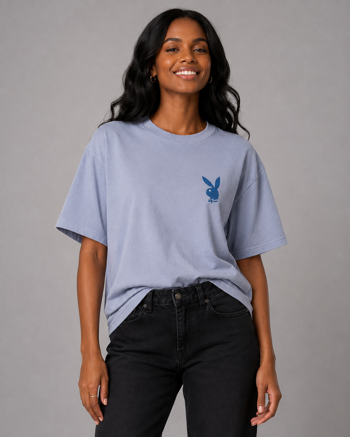 A woman wearing a light periwinkle blue t-shirt with a small blue Playboy bunny logo on the left chest, paired with black jeans, against a solid gray studio background. #Women