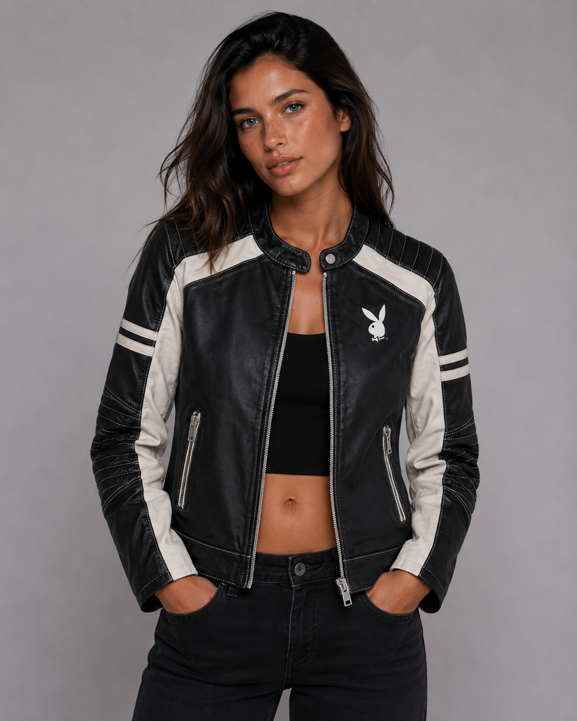 A woman modeling a black and white leather jacket with the Playboy bunny logo on the chest, paired with a black crop top and black jeans against a gray studio background. #Women