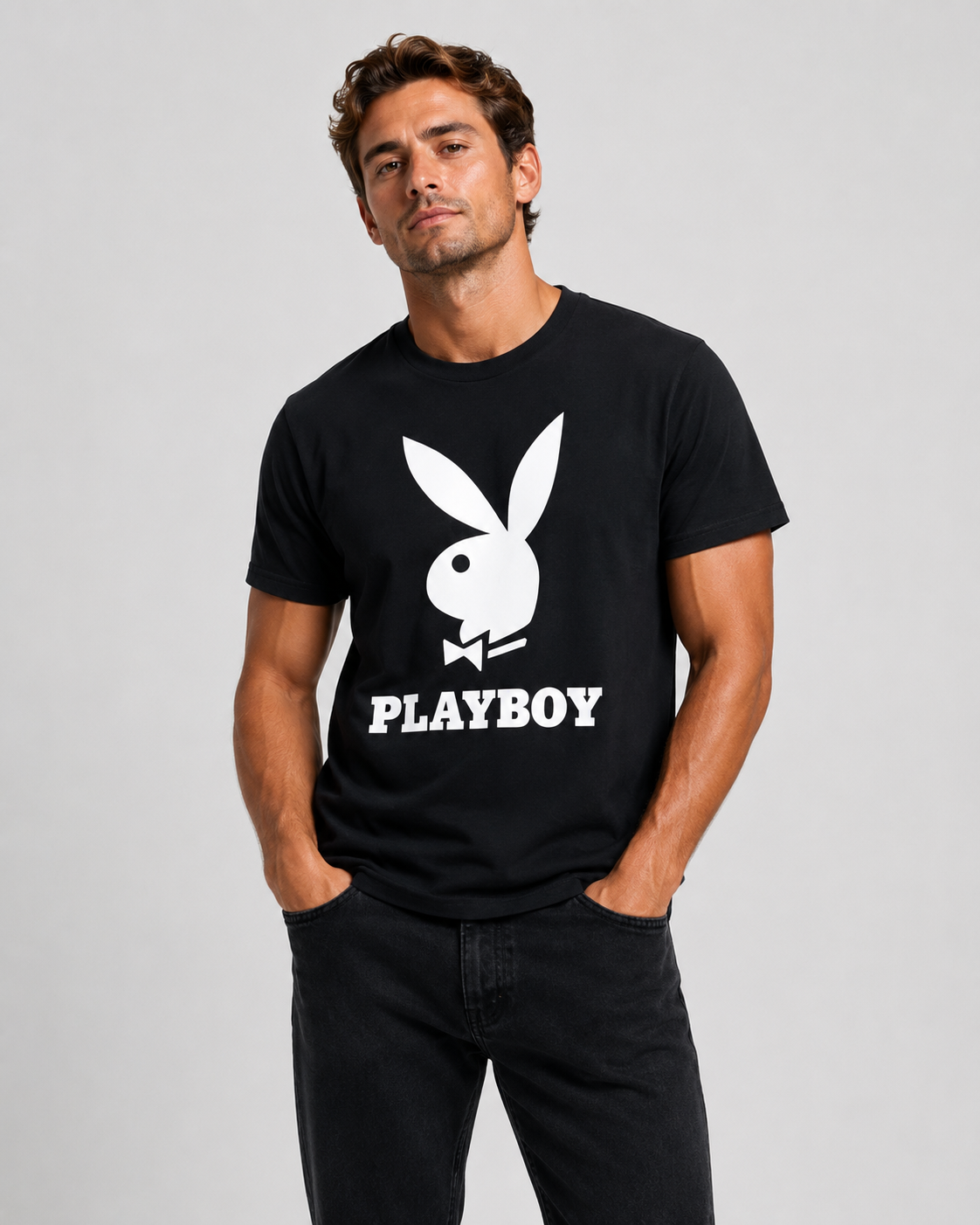 A man wearing a black short-sleeve t-shirt with a large white Playboy bunny logo and the word 'PLAYBOY' printed on the front, paired with black jeans, against a light gray studio background.