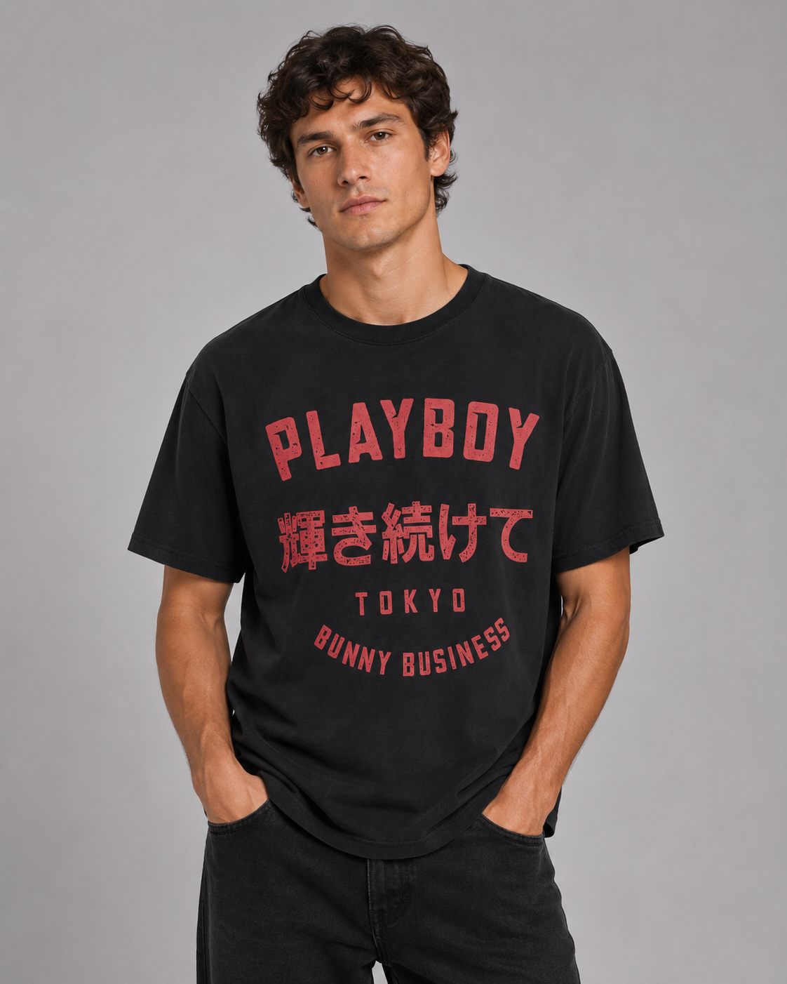 A man wearing a black short-sleeve t-shirt with red graphic text on the front, including 'PLAYBOY' and Japanese characters, posed against a solid gray studio background.
