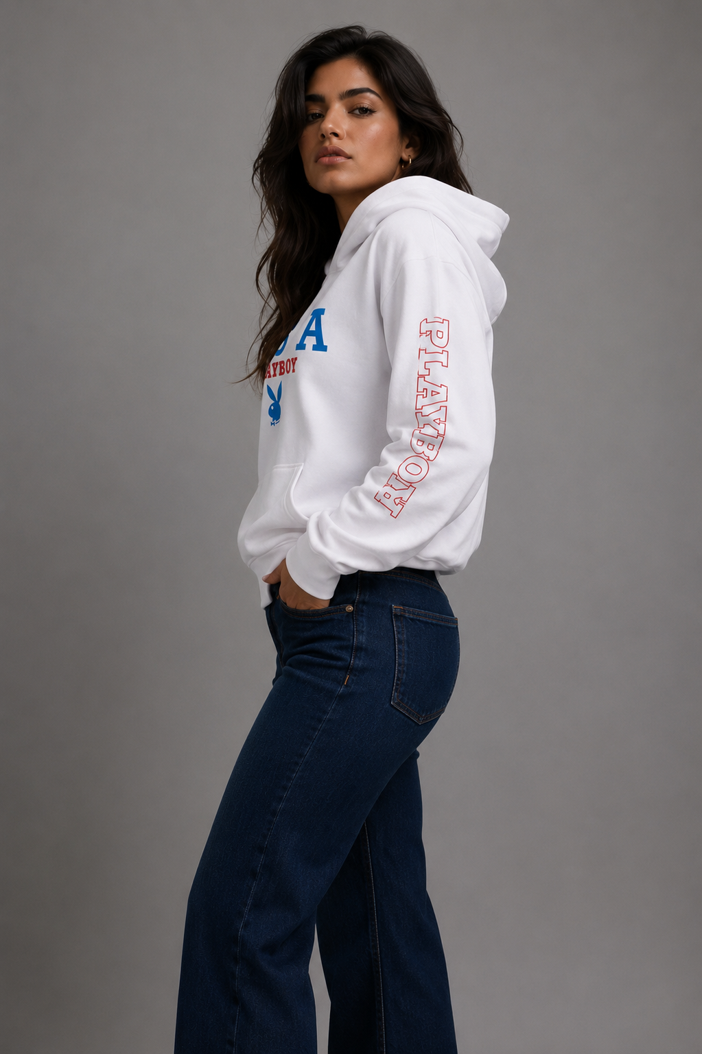 A woman modeling a white pullover hoodie with blue and red graphics, paired with dark blue jeans, against a solid gray studio background. #Women