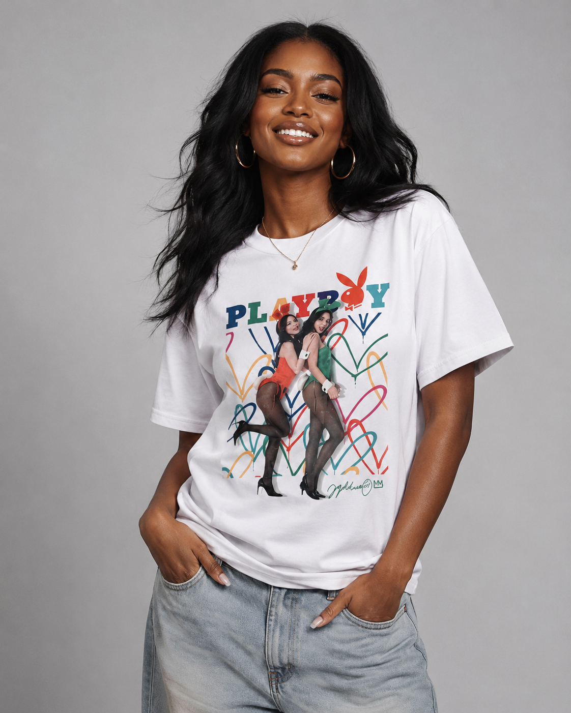 A woman wearing a white Playboy graphic t-shirt with a colorful retro design and logo, paired with light-wash jeans, against a solid gray studio background. #Women