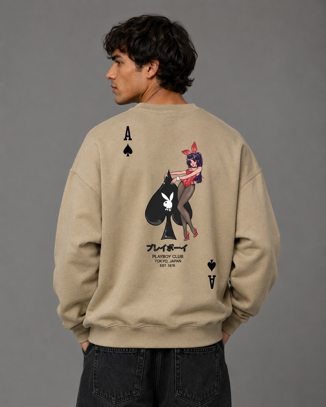 A man wearing a beige crewneck sweatshirt from the back, featuring a graphic of a pin-up girl with a Playboy bunny and the text 'PLAYBOY CLUB FANTASY UNITED EST. 1963' on a gray background.