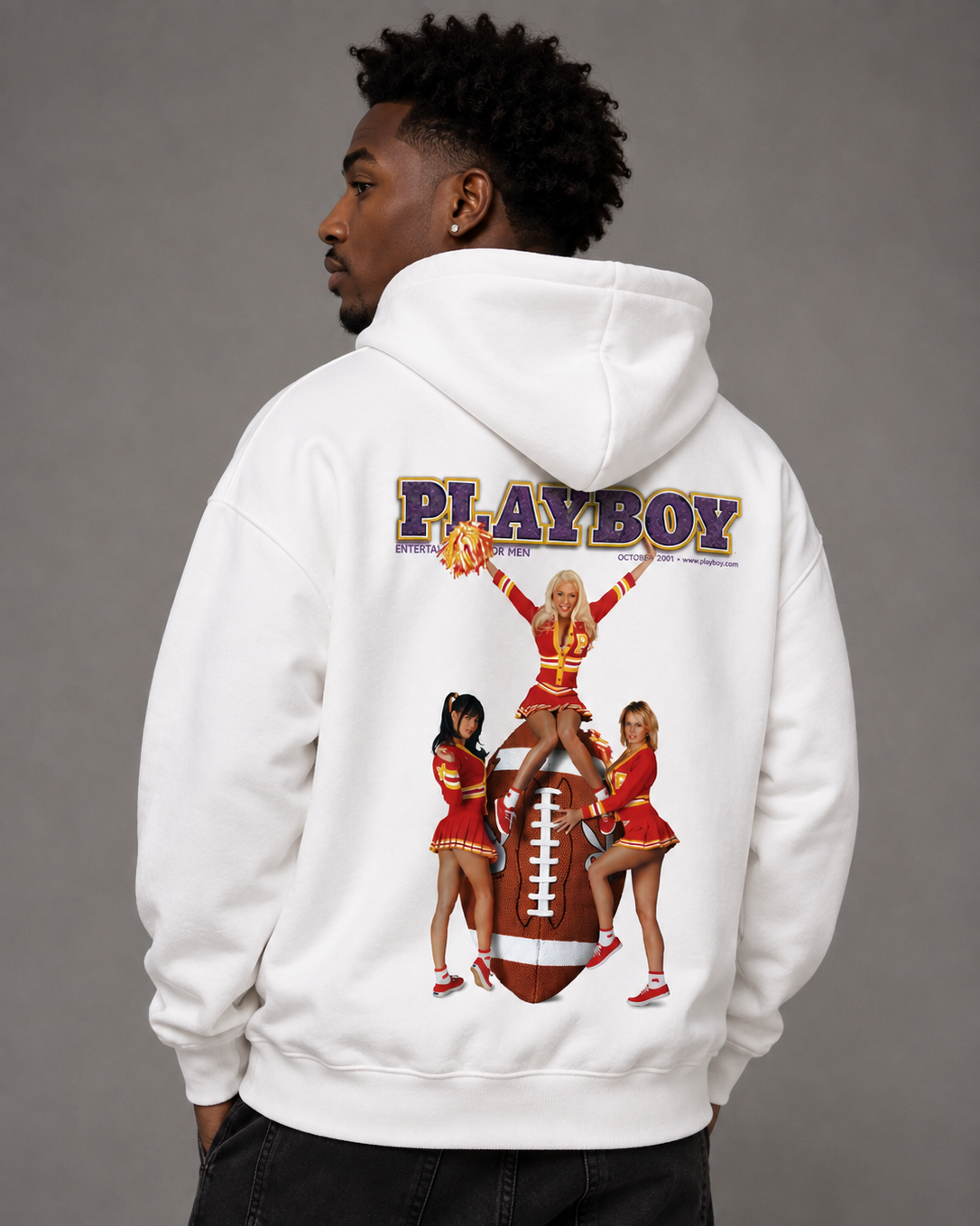 A man wearing a white hoodie from the back, featuring a large graphic print of the Playboy logo above cheerleaders holding a football, against a solid gray studio background.