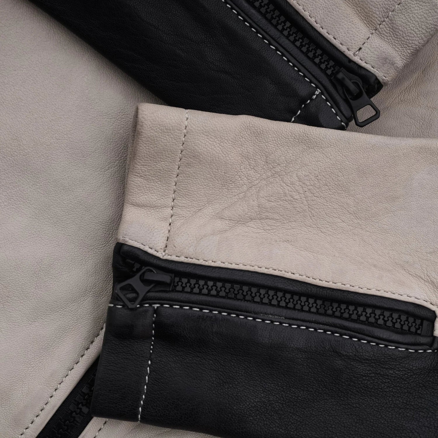 Close-up of black and beige men's leather jacket sleeves with zippers and stitching detail