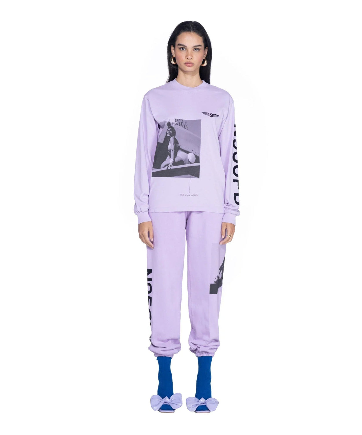 Woman wearing lavender long sleeve graphic t-shirt and matching joggers with photo print and bold lettering, blue socks, and lavender bow sandals.