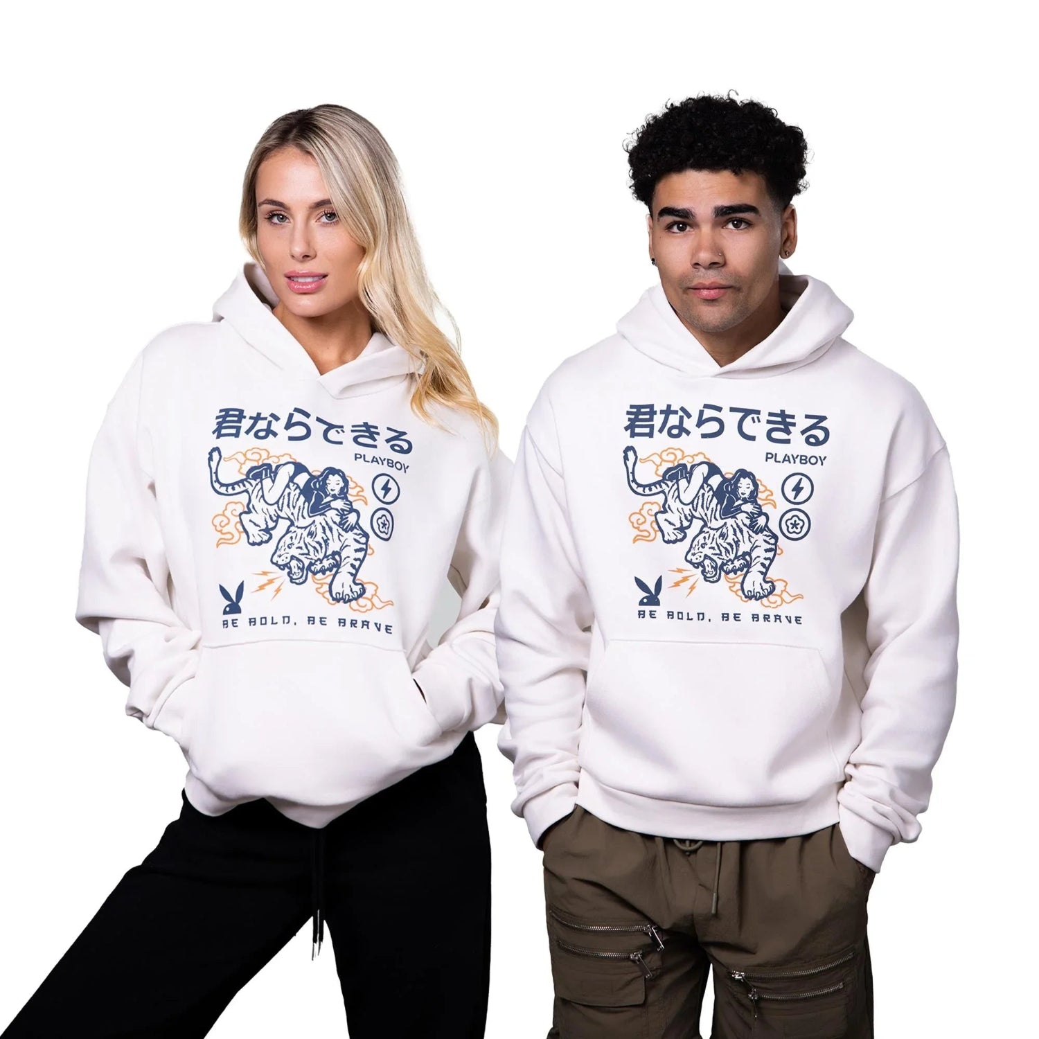 Two models wearing white graphic hoodies with Japanese text, tiger design, and slogan 'Be Bold, Be Brave'.