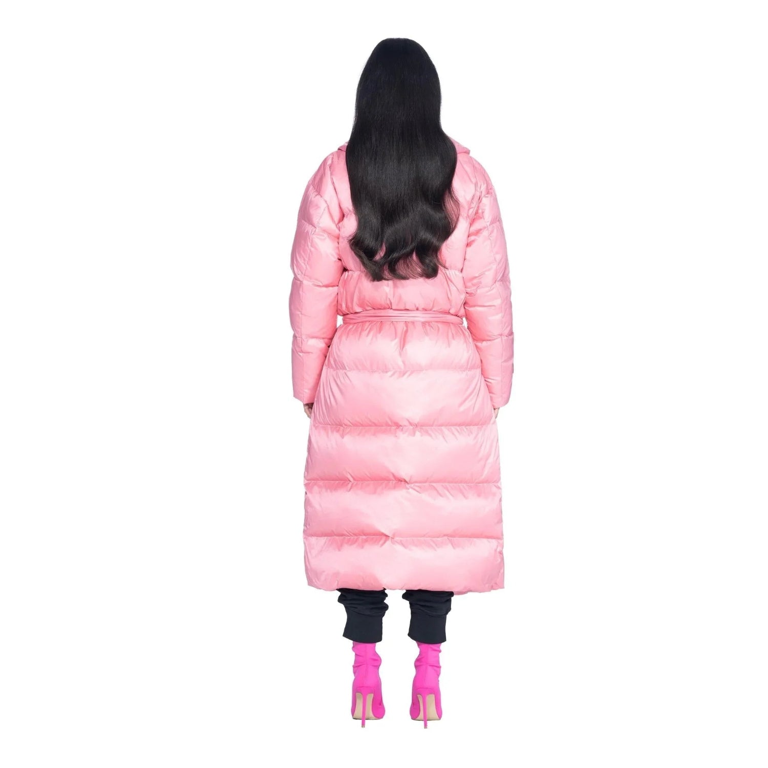 Woman wearing pink belted long puffer jacket, black pants, and pink heels, back view